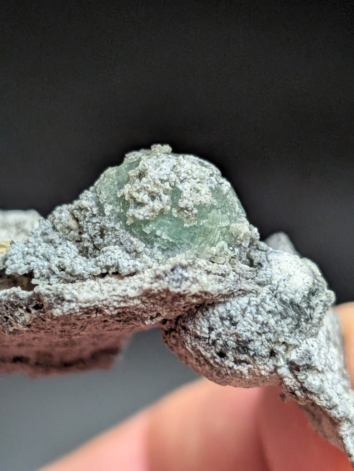 A translucent green gemstone nestled within a rough, grayish matrix of rock.