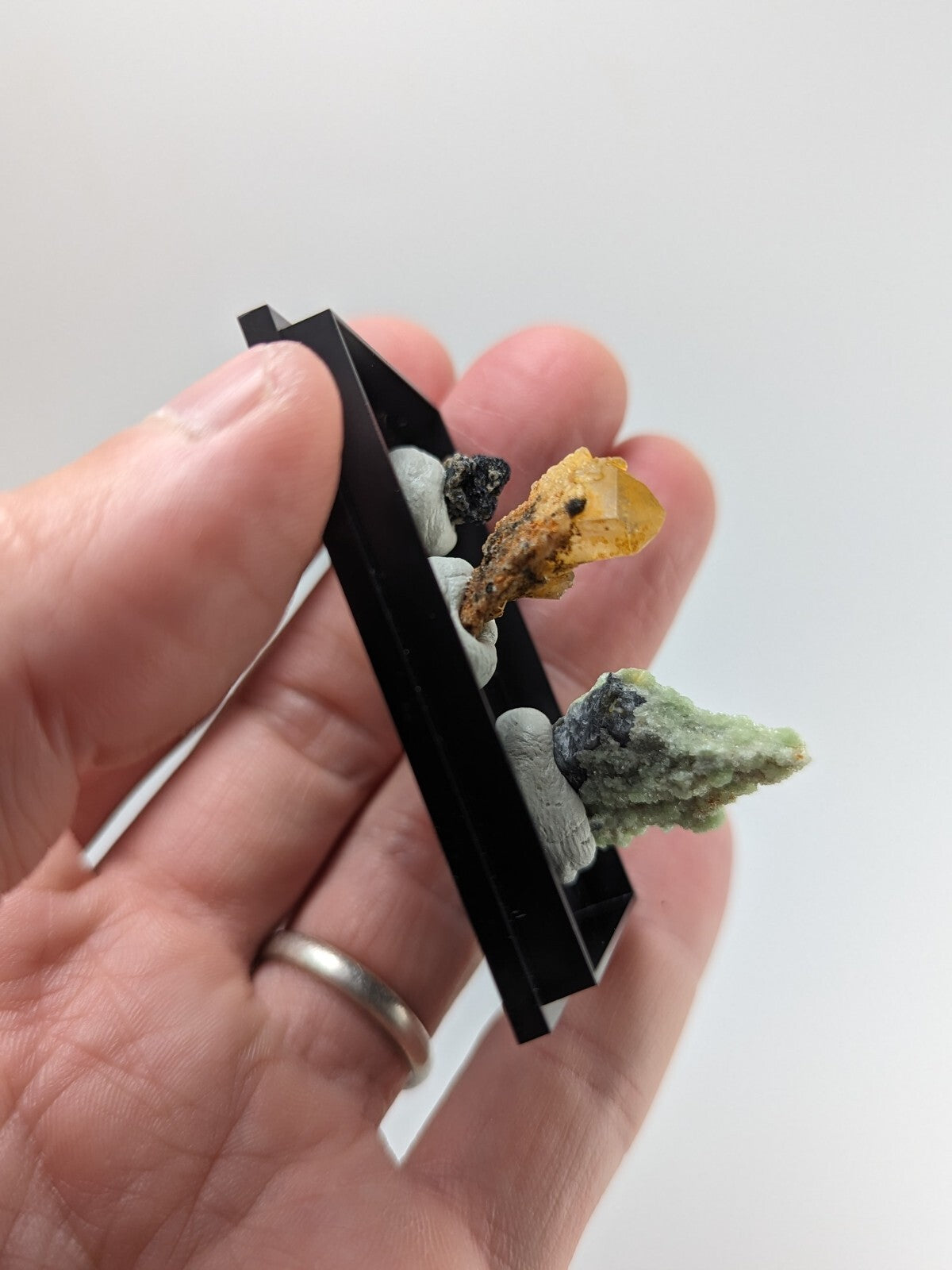 Black rectangular mineral display case holding a collection of colorful, naturally occurring rock specimens.