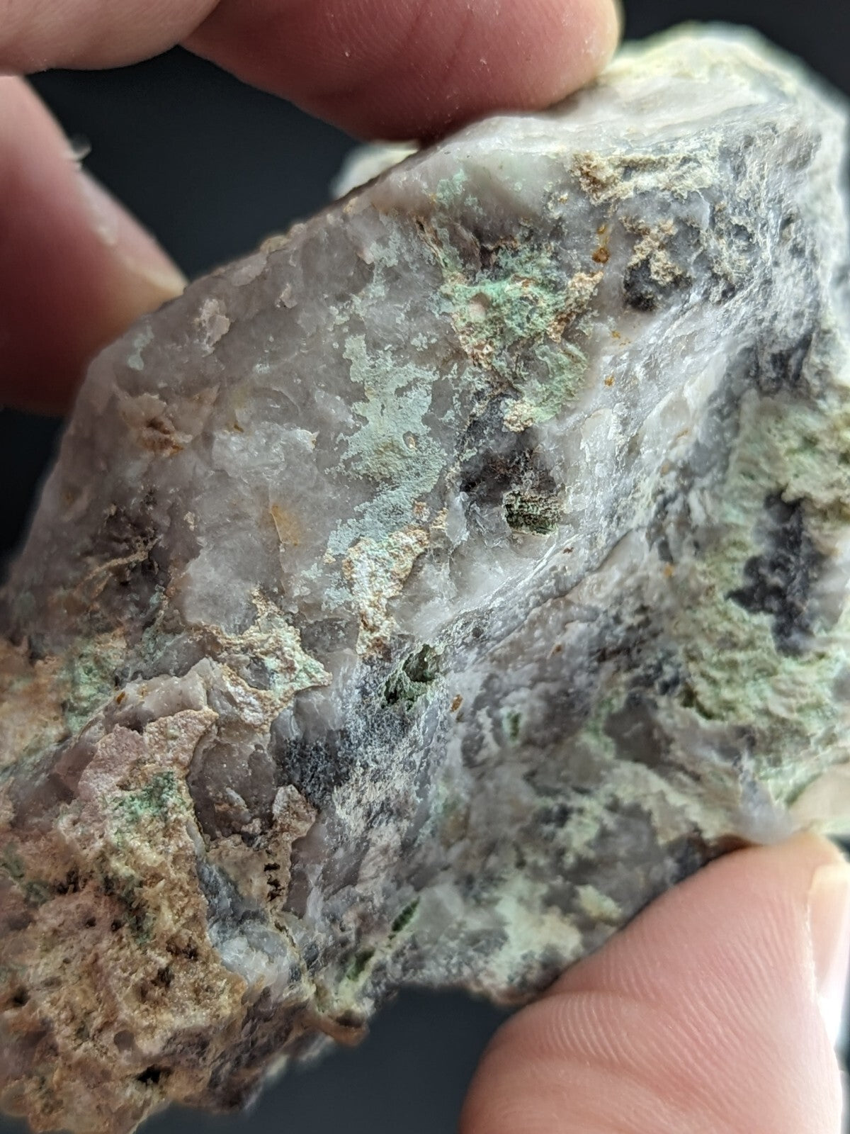 A rough, translucent gray rock with patches of green and black mineral deposits.
