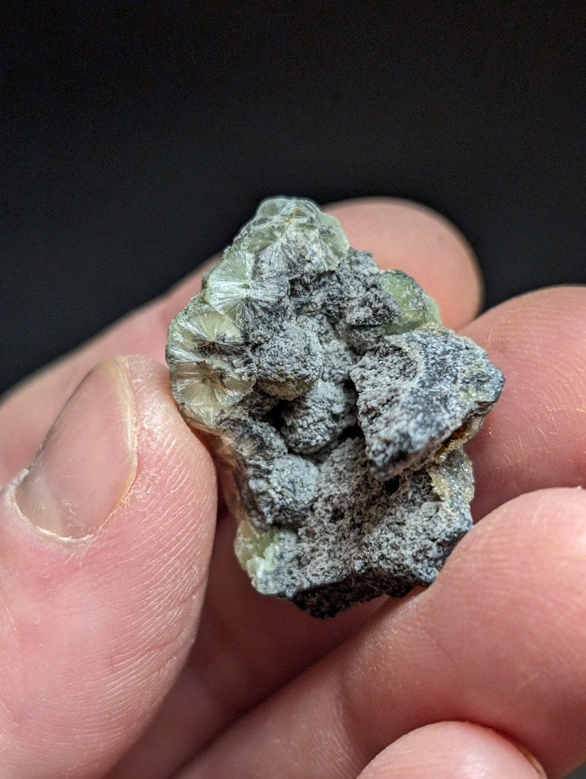 A rough, translucent green mineral specimen with a grayish-black crusty coating.