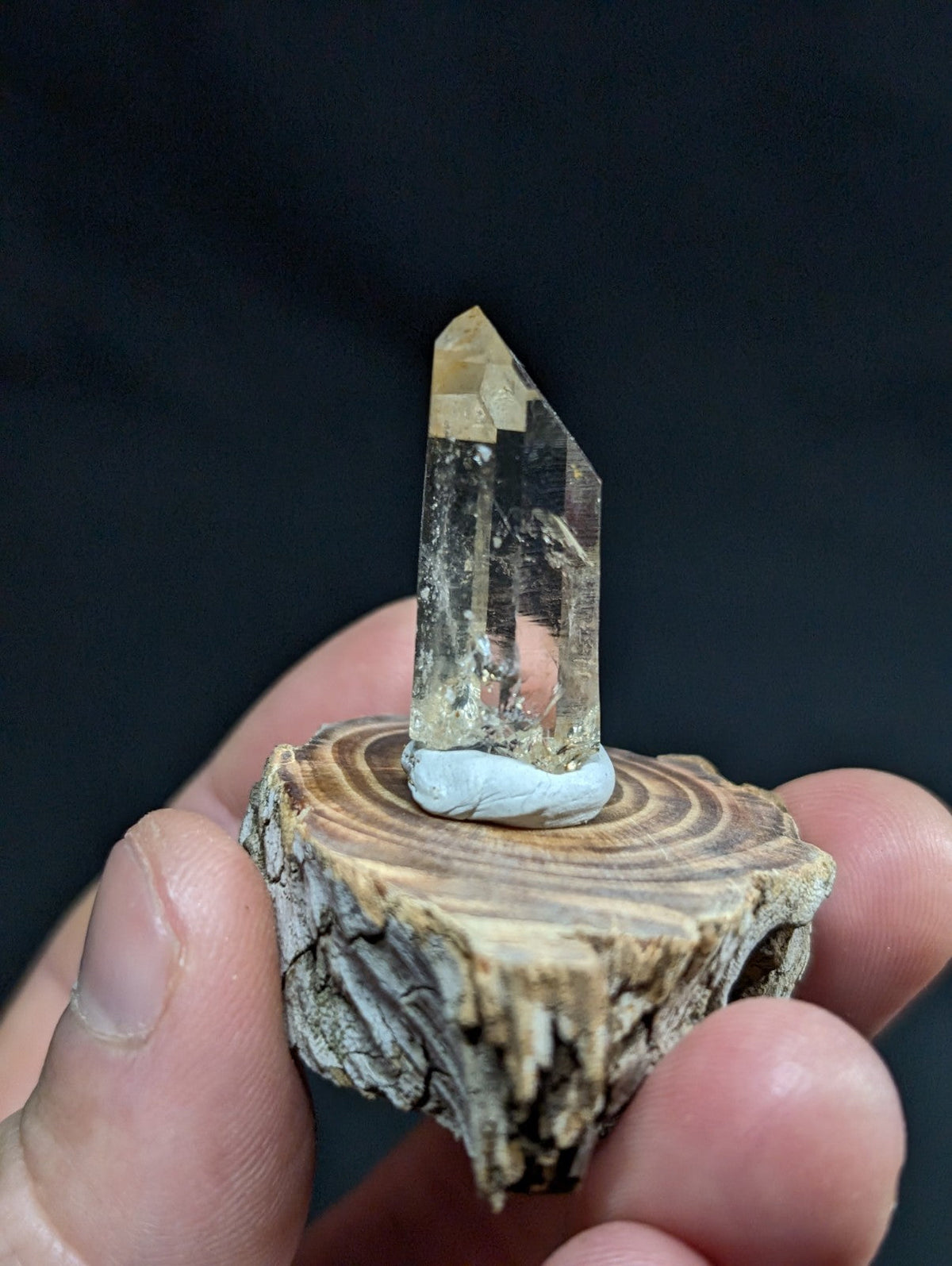 A translucent, pale yellow crystal with a pointed tip and visible internal inclusions stands upright on a small, circular wooden base.