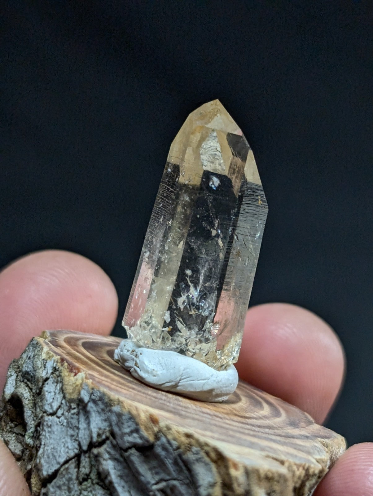 A translucent yellowish quartz crystal with a pointed tip, held upright on a small wooden base.