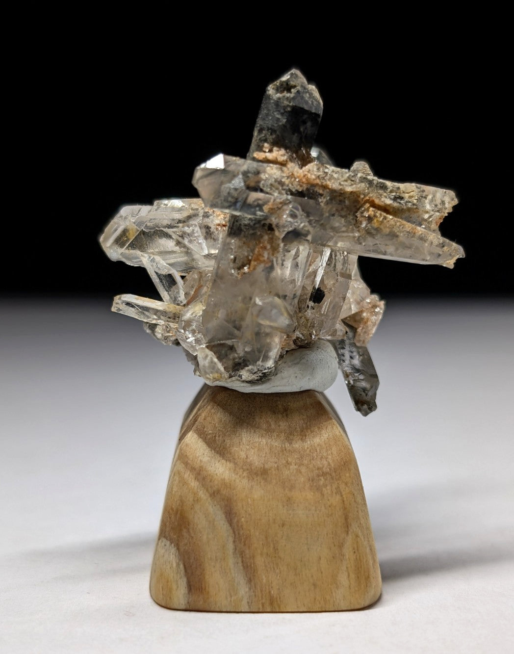 A clear quartz crystal cluster with sharp, translucent points and darkened tips rests on a light brown wooden base.