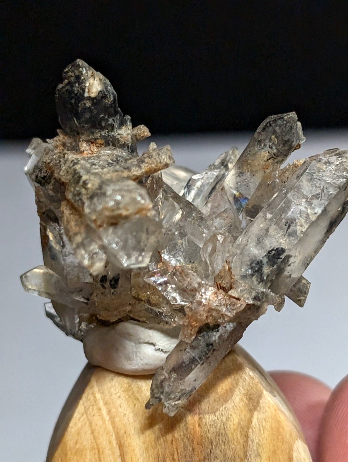 A cluster of translucent quartz crystals with clear, sharp facets and dark inclusions rests atop a wooden display stand.