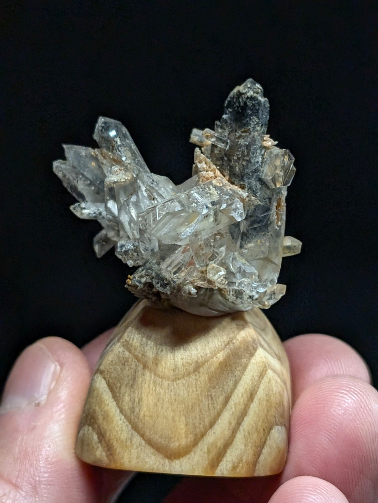A clear, faceted crystal cluster with translucent and slightly cloudy formations rests atop a smooth, light-brown wooden base.