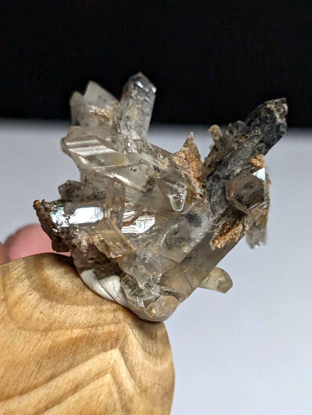 A cluster of translucent, faceted quartz crystals with a mix of clear and smoky hues, held in place by a wooden display stand.