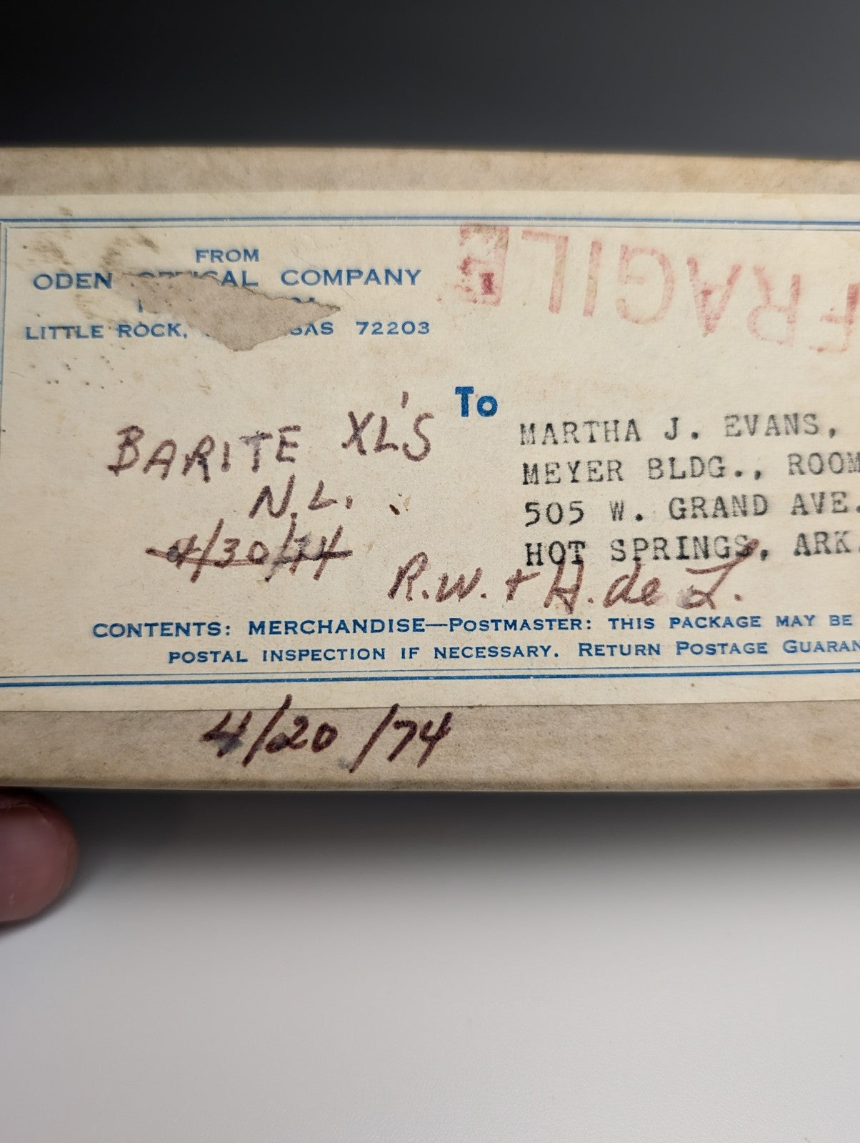 A beige postal shipping label with blue printed text and black ink markings on the back of a barite crystal case