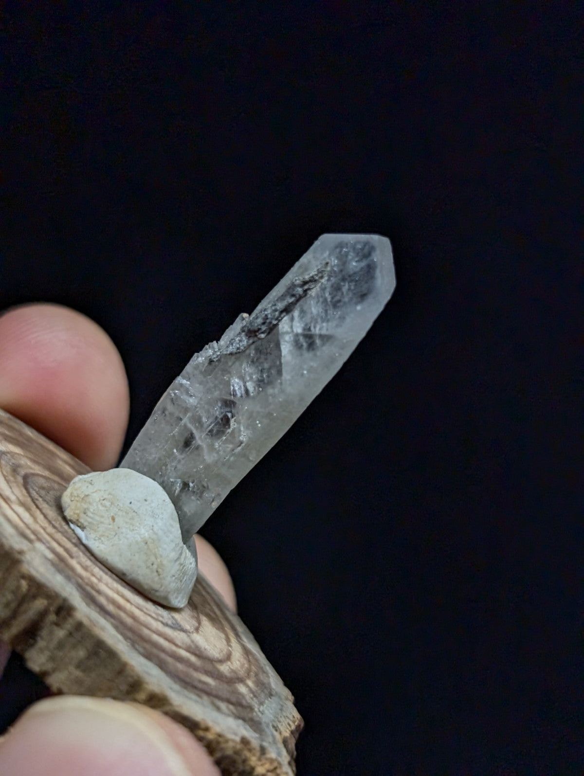 A translucent quartz crystal with a pointed tip and internal inclusions, held upright on a rustic wooden base.