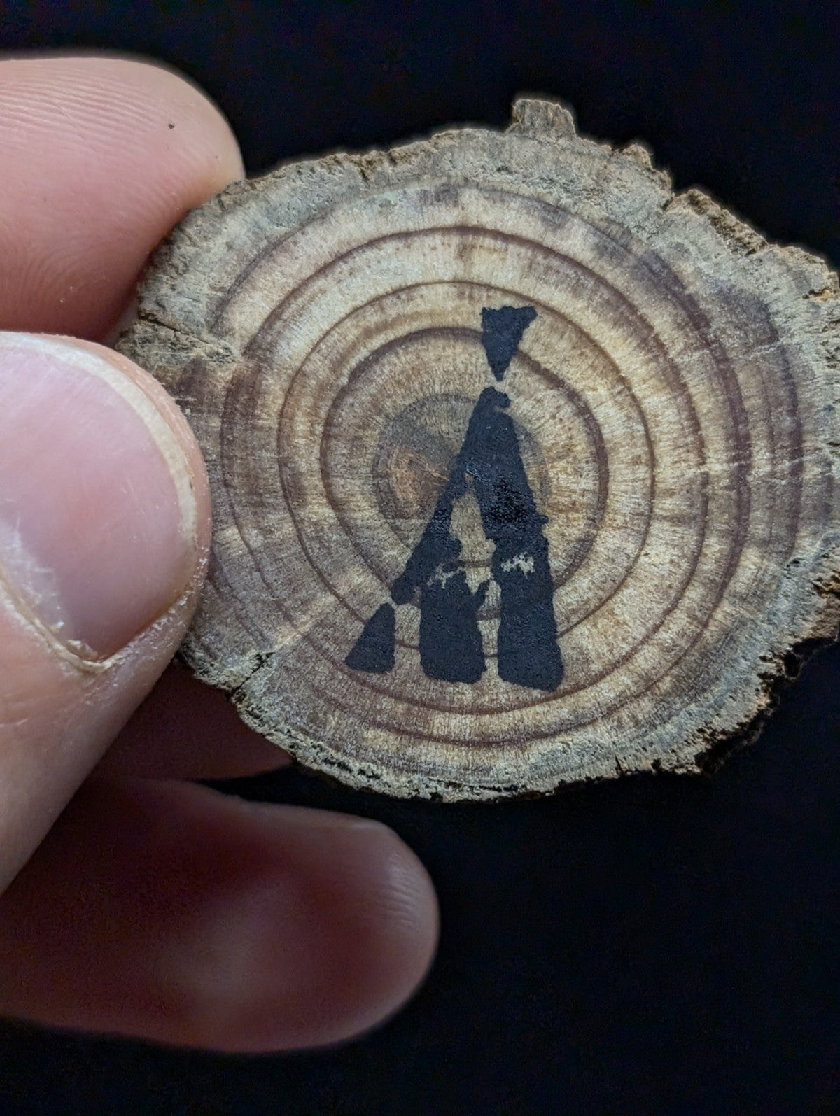 A rustic circular wood slice pendant featuring a dark blue painted silhouette of two figures against its natural grain.