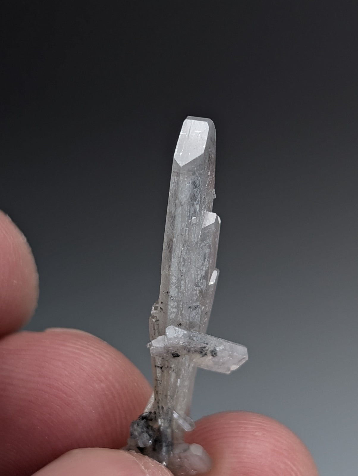 A translucent clear quartz crystal cluster with tall central spike held between fingers from magnet cove arkansas
