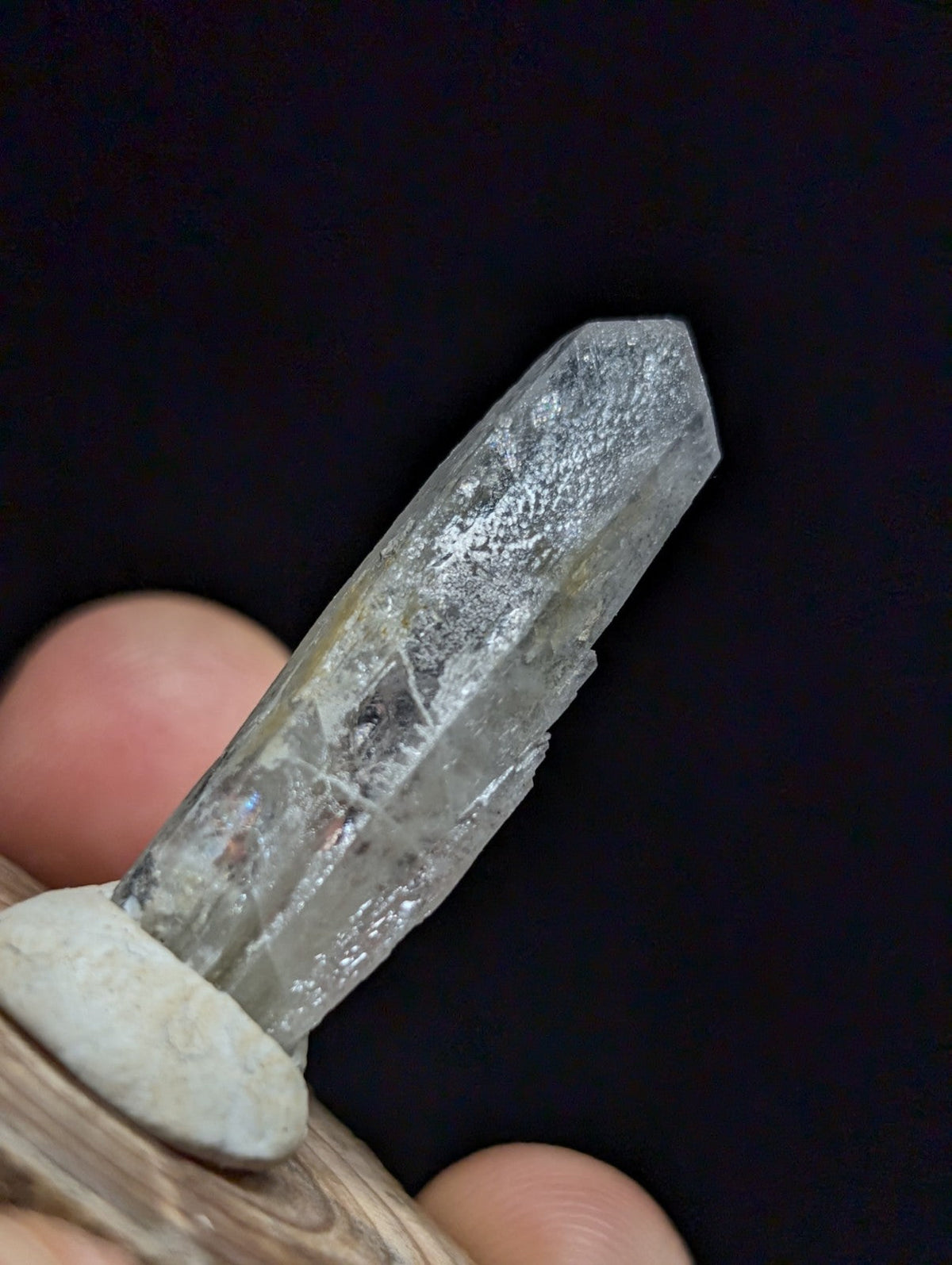 A translucent, clear quartz crystal with subtle internal inclusions and a pointed tip, held securely by a wooden display stand.