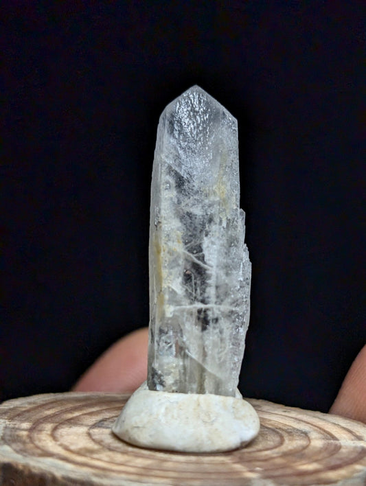A clear, translucent quartz crystal with natural striations and a pointed tip, displayed on a white ceramic stand.