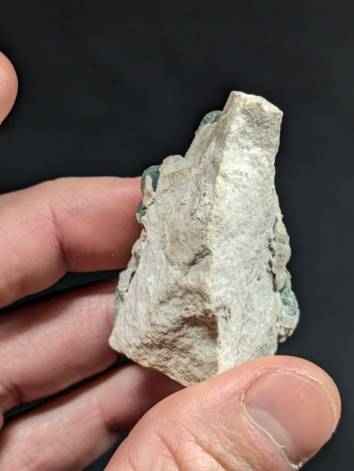 A rough, irregularly shaped stone with a pale gray surface and patches of greenish patina.