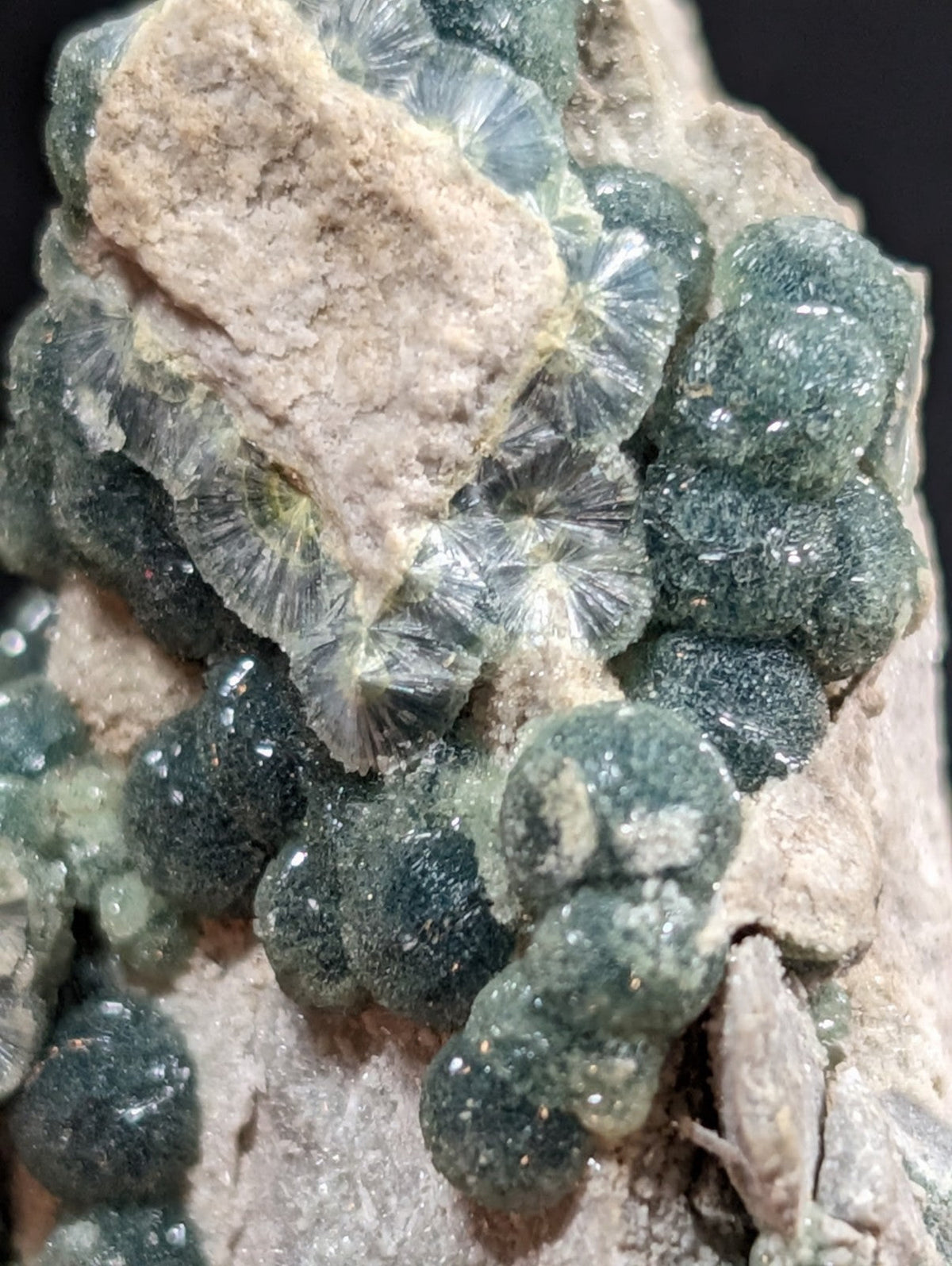 A cluster of translucent, greenish-blue druzy crystals with a radial, fan-like internal structure embedded in light brown rock.