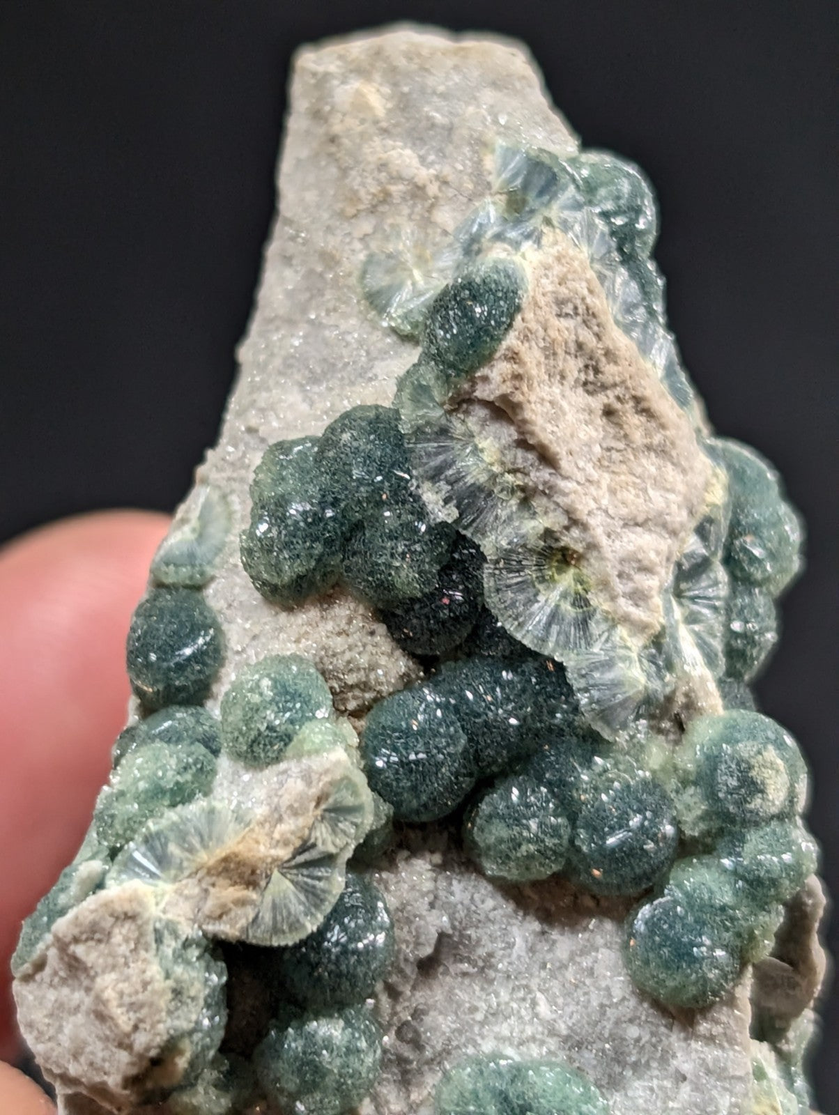 A cluster of translucent green, spherical crystals with a glittering surface grows from a rough gray rock matrix.