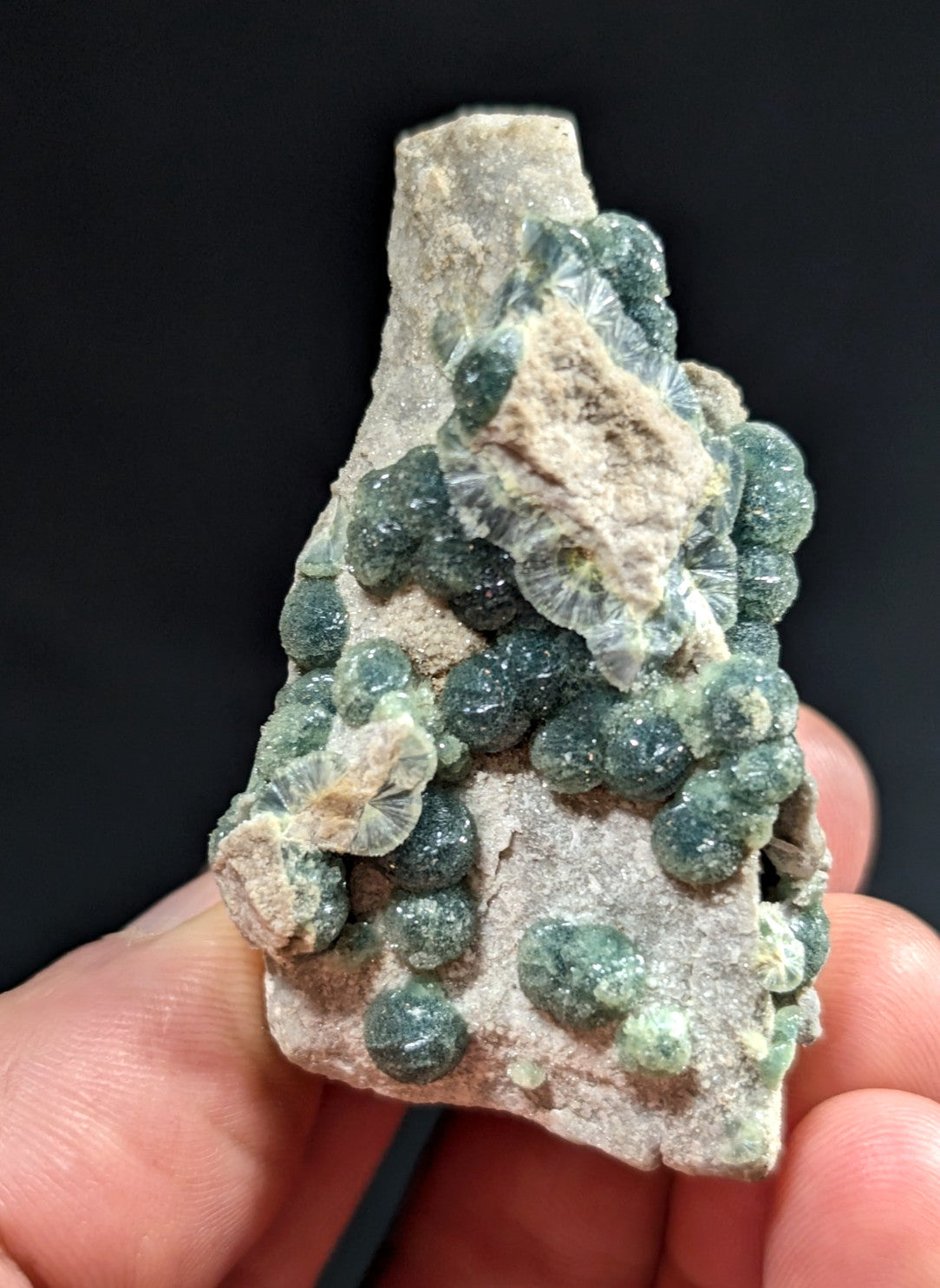 A cluster of translucent green spherical crystals growing from a rough, light-colored rock matrix.