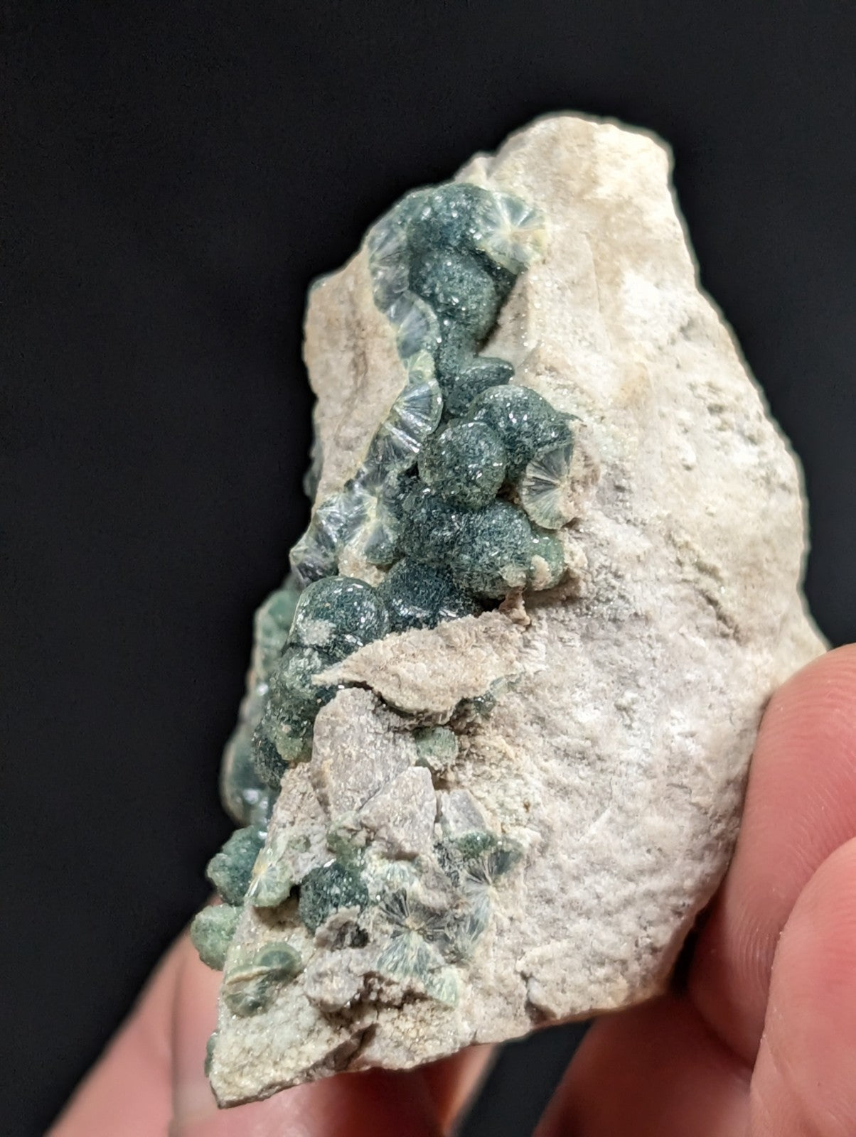 A cluster of translucent green crystals grows in a rough, light-colored rock matrix.