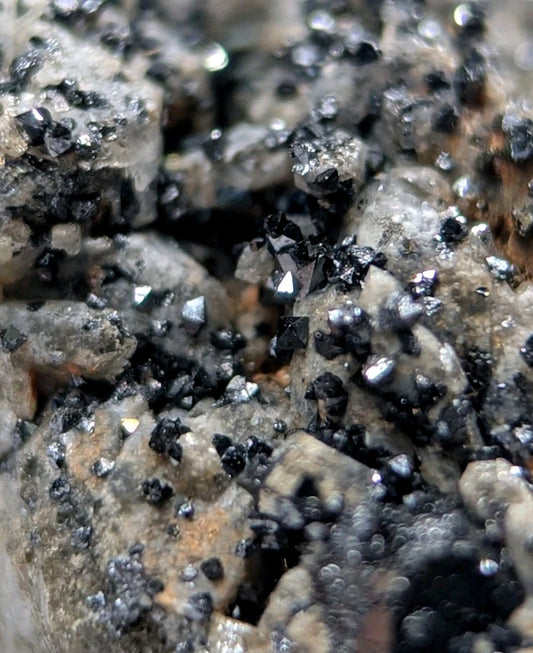 A cluster of dark, faceted crystals embedded in a rough, grayish rock matrix.
