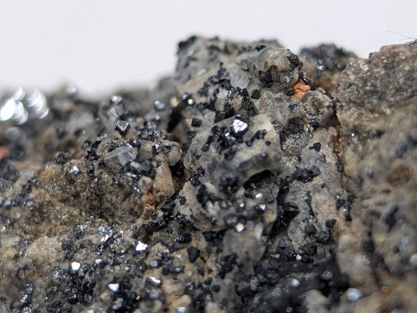 A close-up of a mineral specimen featuring dark, metallic-looking crystals embedded in a grayish matrix with specks of black and brown.