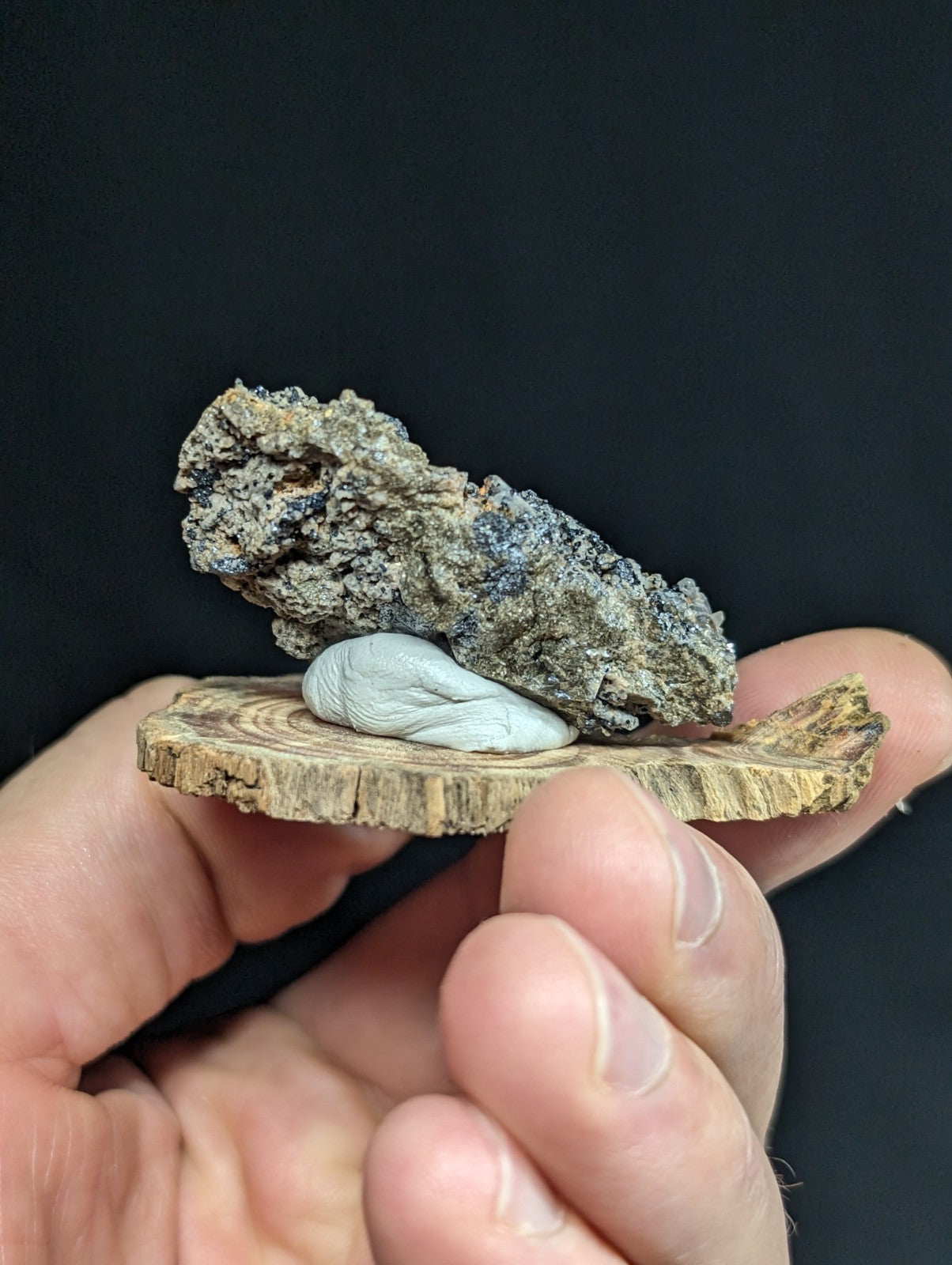 A delicate, pale blue carved stone figurine rests atop a rough-textured gray rock on a natural wood slice.