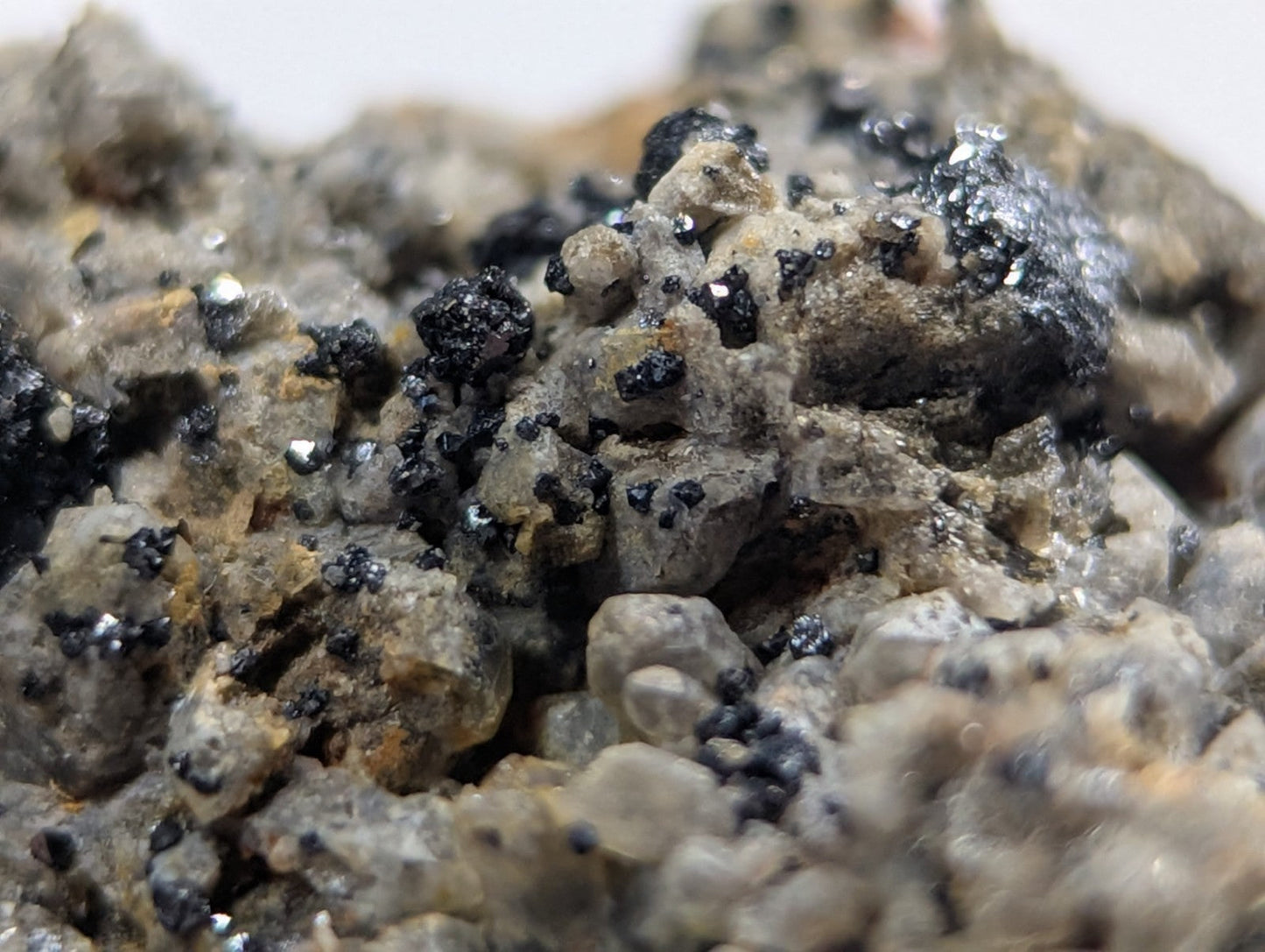 A rugged, grayish mineral specimen with scattered black metallic inclusions and subtle yellowish undertones.