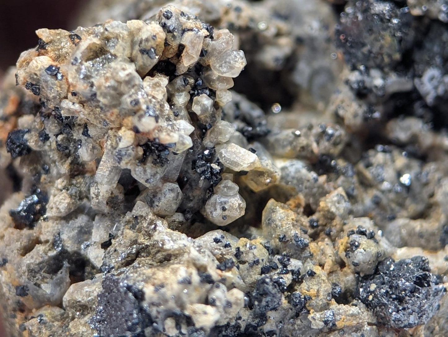 A cluster of translucent, crystalline minerals with specks of black and yellowish-brown matrix.