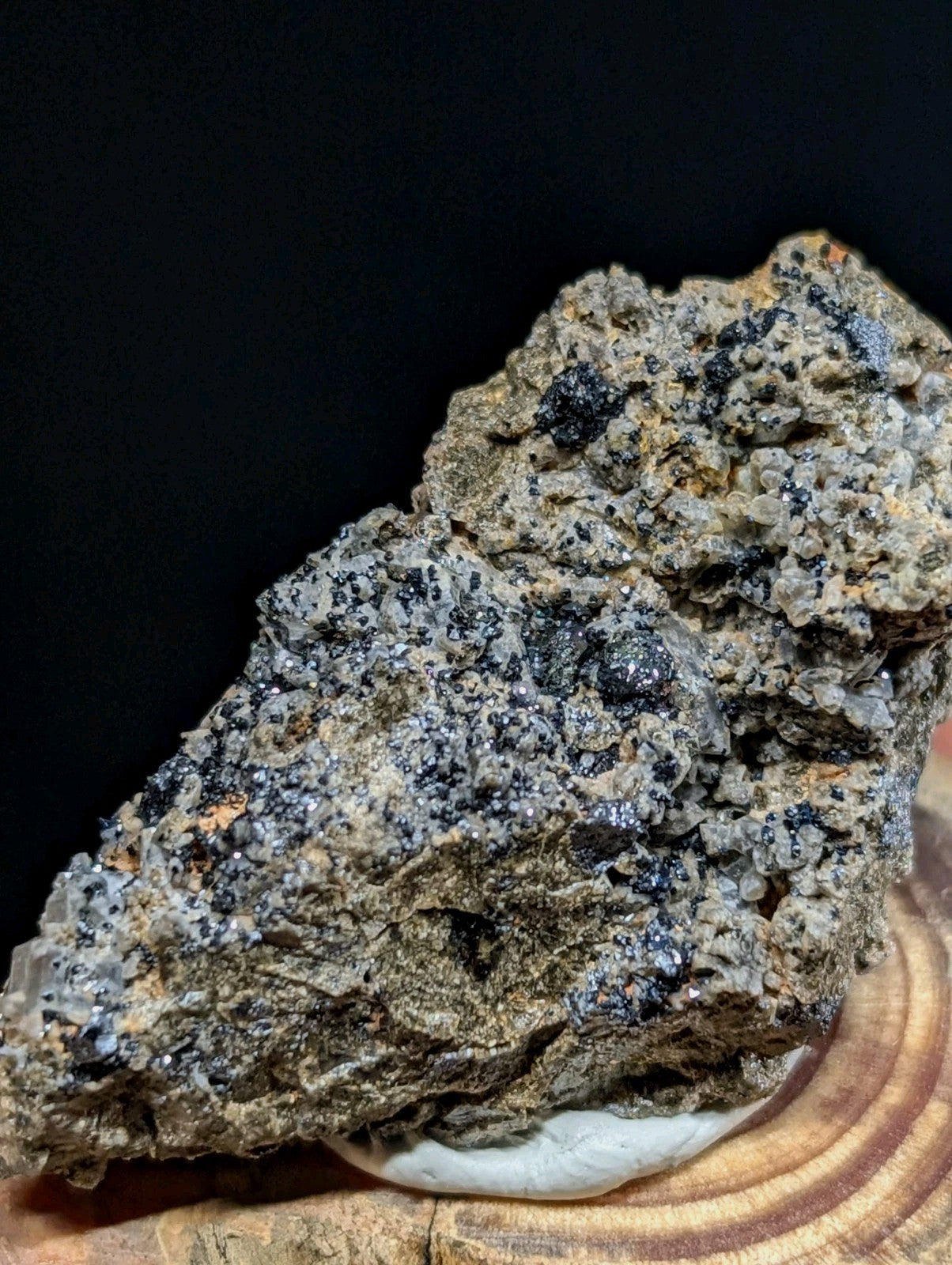 A rugged, textured mineral specimen with a mottled gray and black surface featuring crystalline formations.