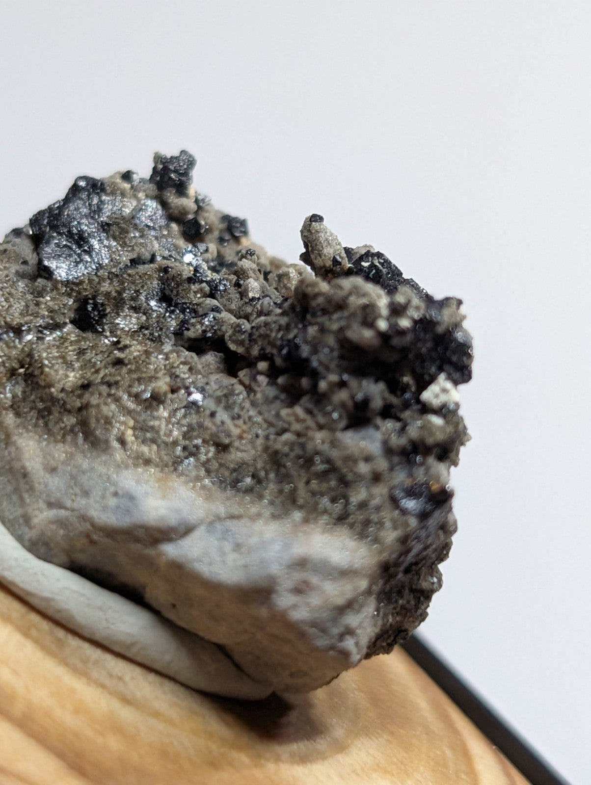 A rugged, naturally occurring mineral specimen with a textured surface featuring dark gray and black crystalline formations atop a lighter, weathered base.