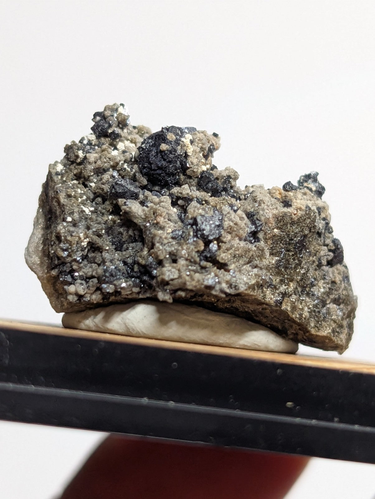 A rugged, irregularly shaped mineral specimen with a textured surface featuring dark black inclusions and speckles of grayish-white crystals.