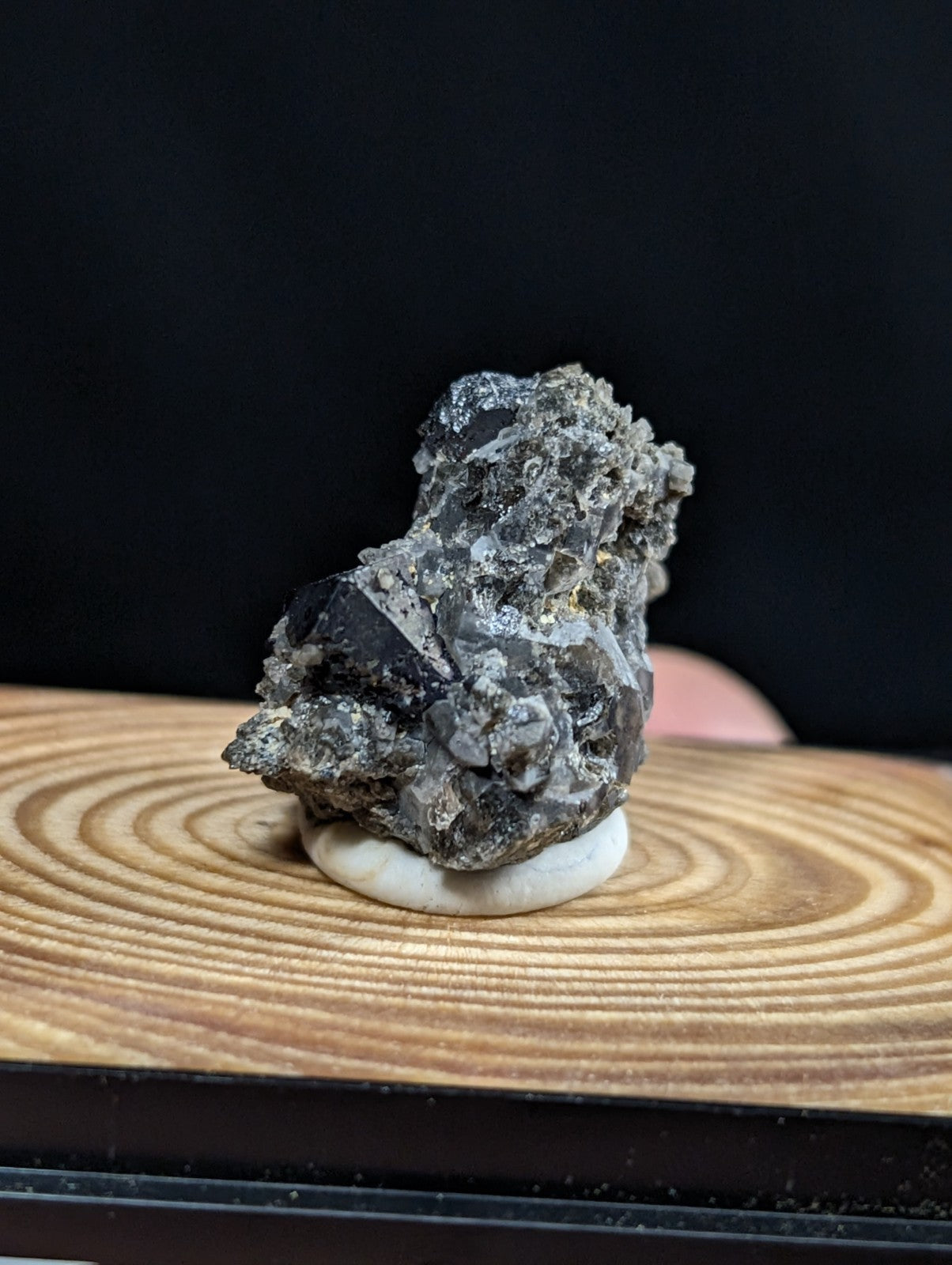 A dark gray, rough-textured mineral specimen with crystalline formations displayed on a white circular base.