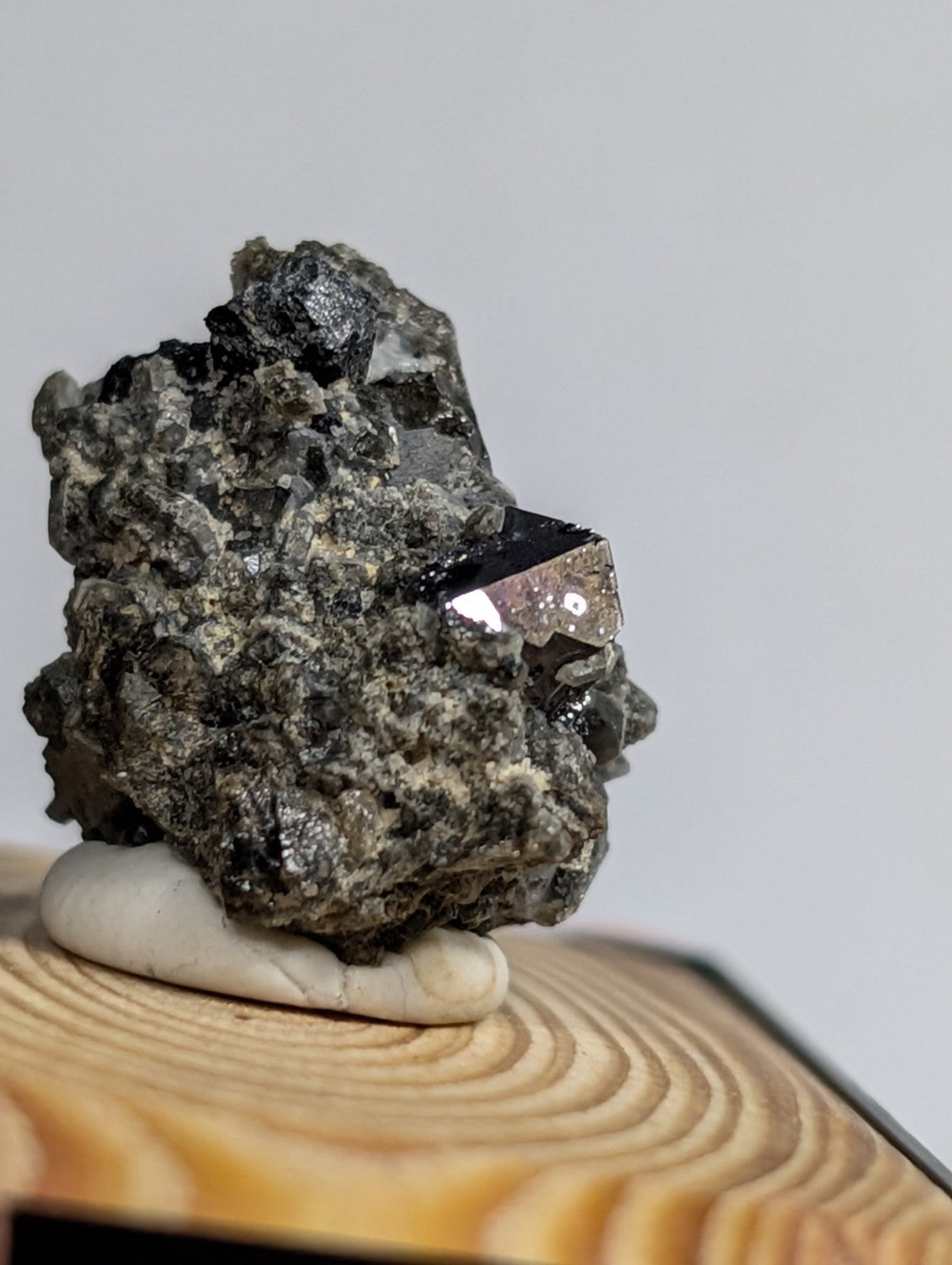 A dark, rough-textured mineral specimen with a prominent metallic sheen and crystalline facets rests on a smooth white base.