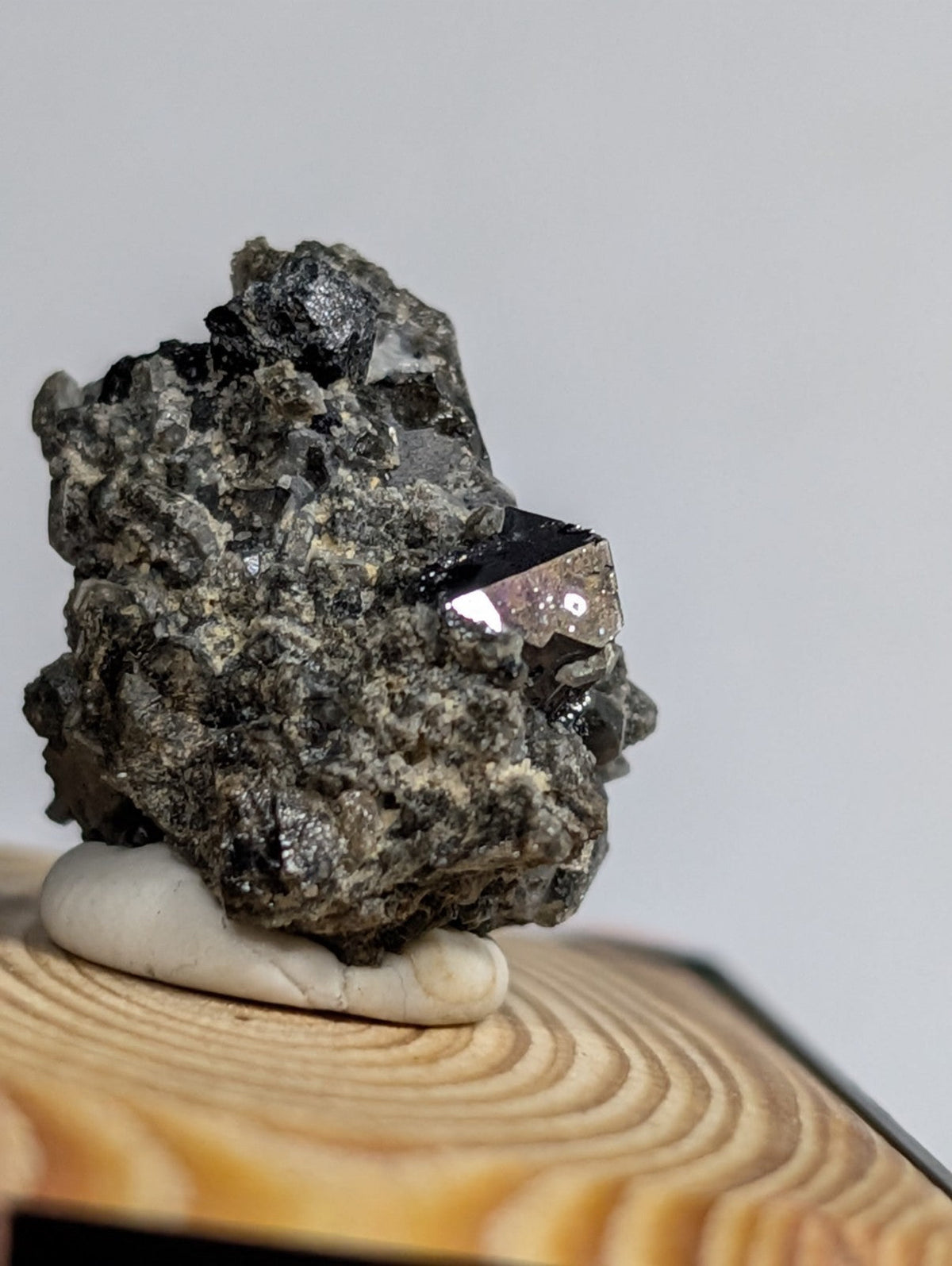 A dark, rough-textured mineral specimen with a prominent metallic sheen and crystalline facets rests on a smooth white base.