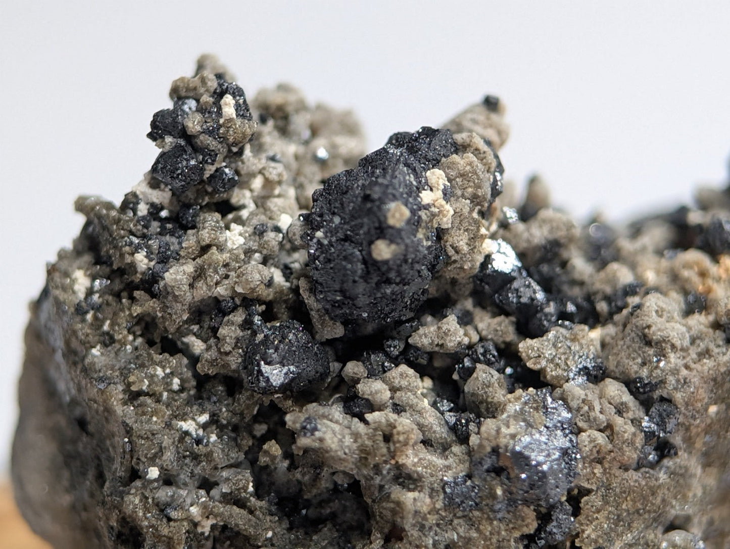 A rugged, textured mineral specimen featuring dark black and grayish-brown crystalline formations with scattered metallic sheen.