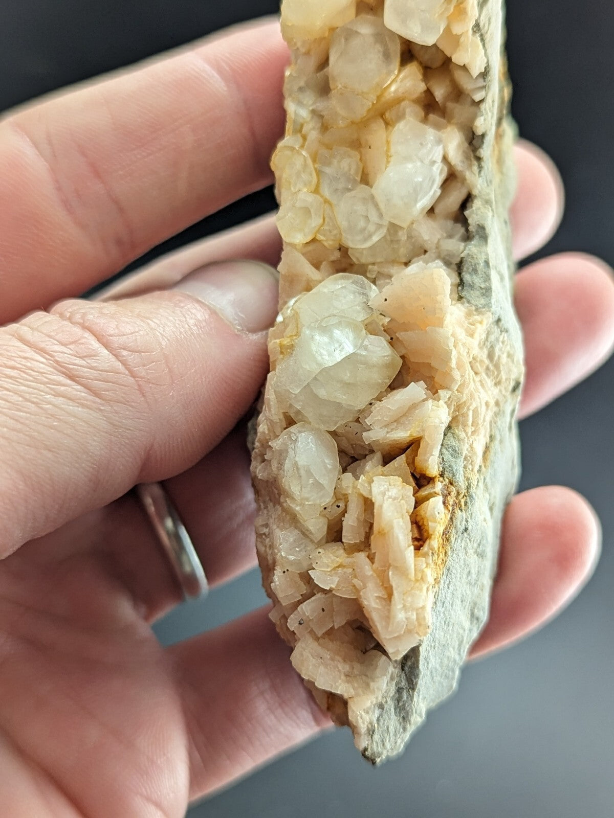 A hand holds a geological specimen featuring translucent, pale yellow to white crystalline formations growing from a rough, grayish rock matrix.