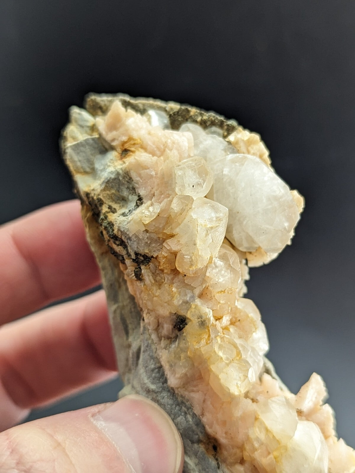 A translucent, pale yellowish-white quartz crystal cluster growing from a dark gray rock matrix.