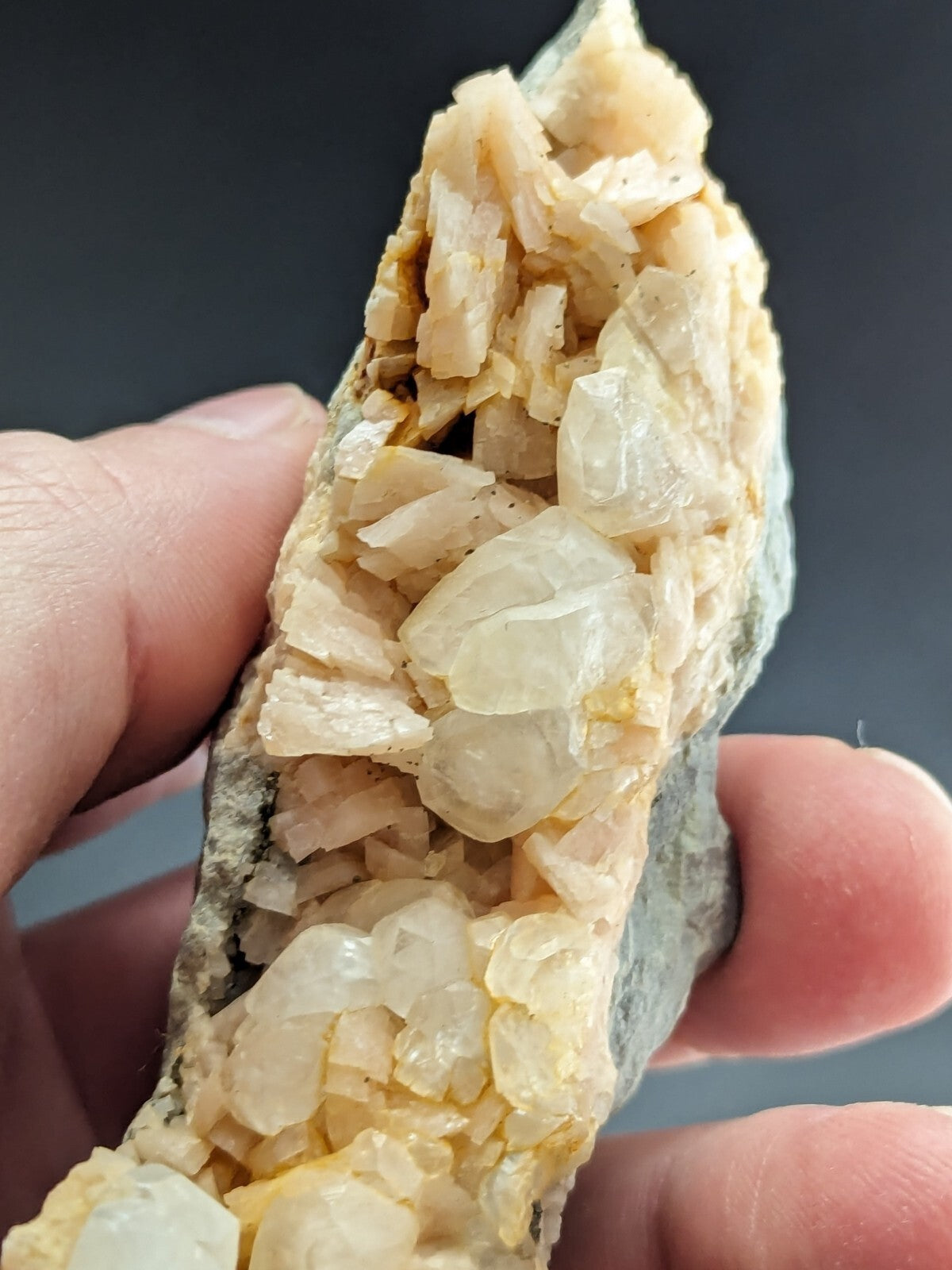 A hand holds a geode with translucent, pale yellow crystals growing from a dark gray rock matrix.