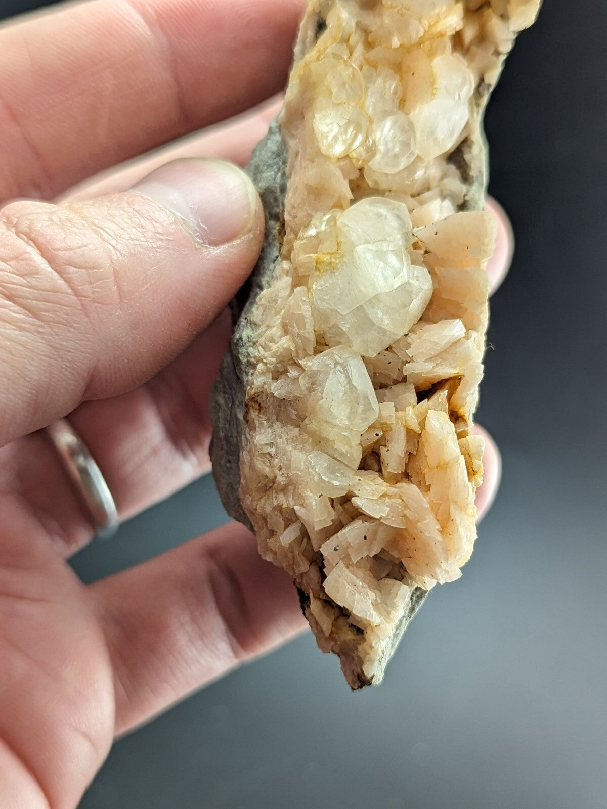A hand holds a geode with translucent, pale yellowish-white quartz crystals growing from a dark gray rock matrix.