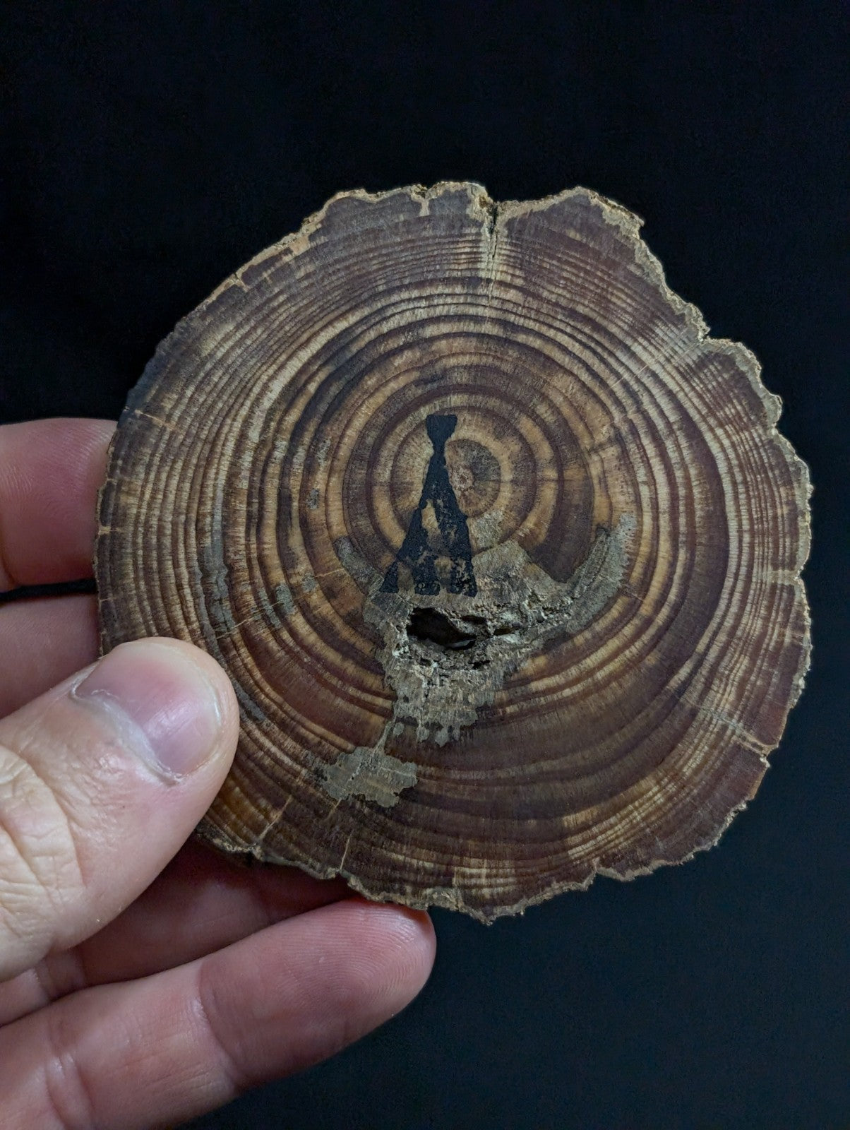A rustic, circular wooden slice with visible growth rings and a dark silhouette of a figure in meditation etched into its surface.