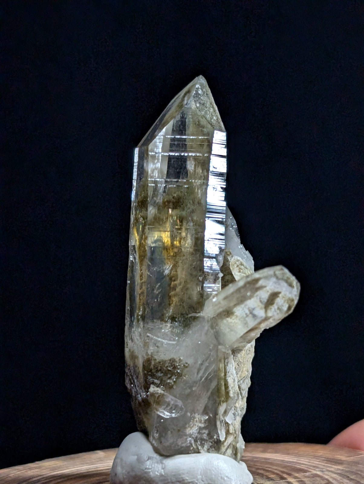 A translucent, pale yellow-green quartz crystal with a pointed tip and visible internal striations stands upright on a white base.
