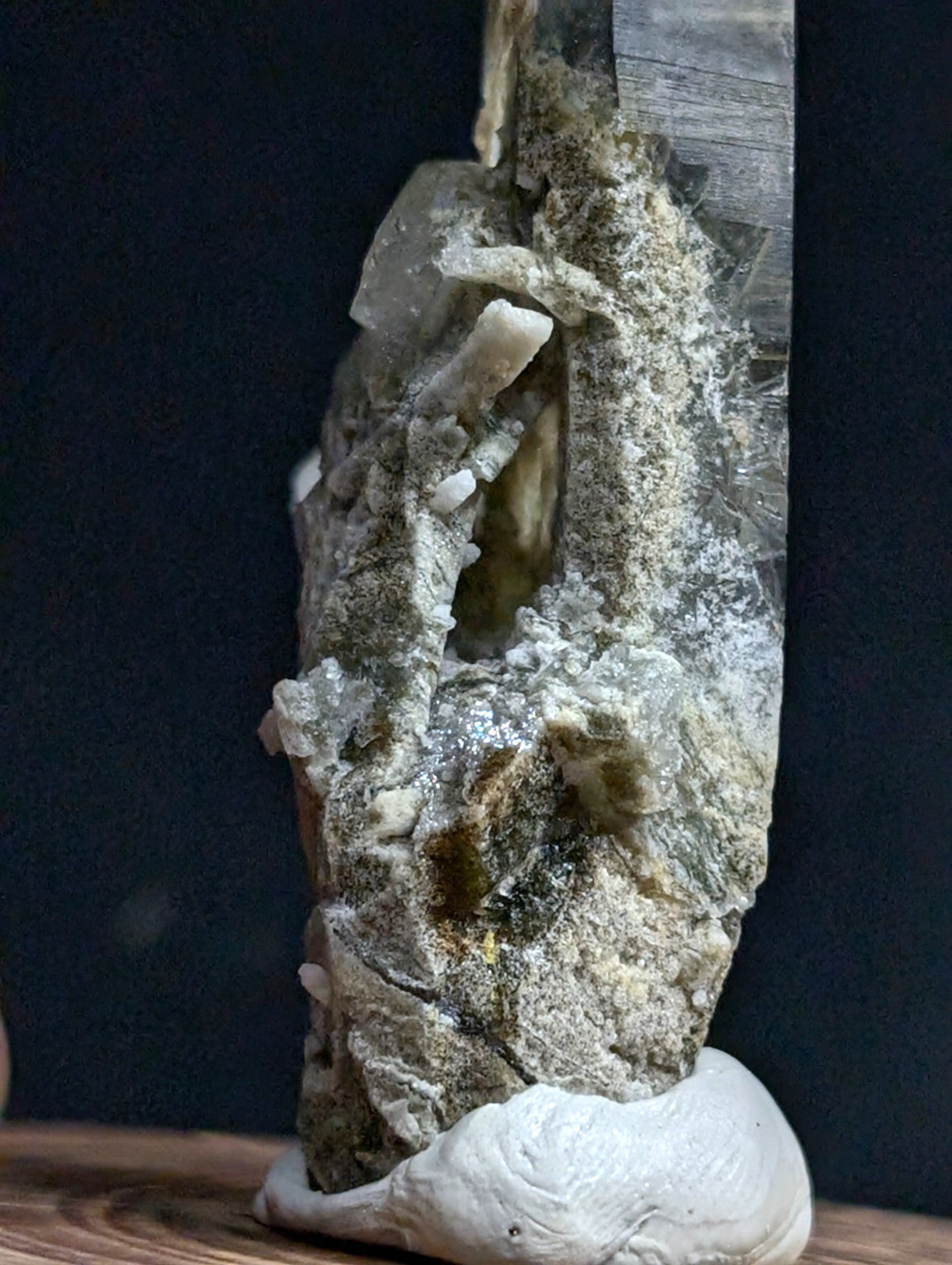 A translucent, crystalline mineral specimen with a rough, textured surface and earthy greenish-gray veining.
