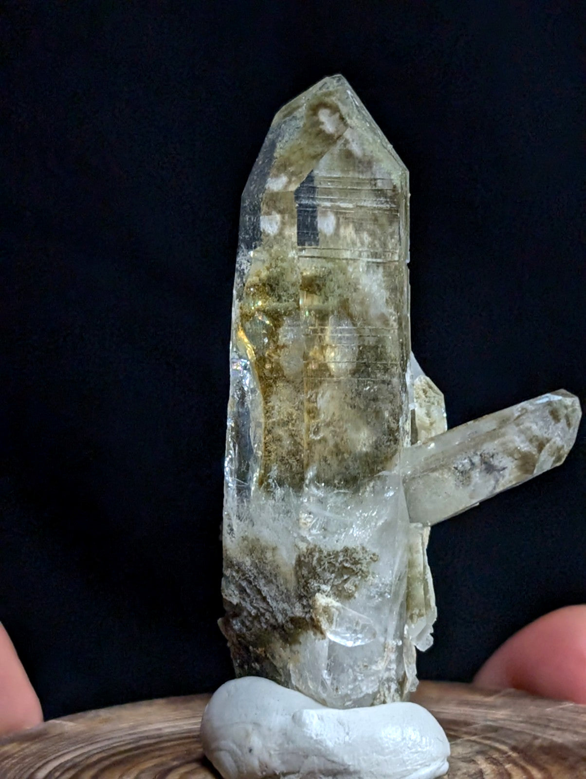 A translucent quartz crystal cluster with greenish inclusions and a pointed, faceted top.