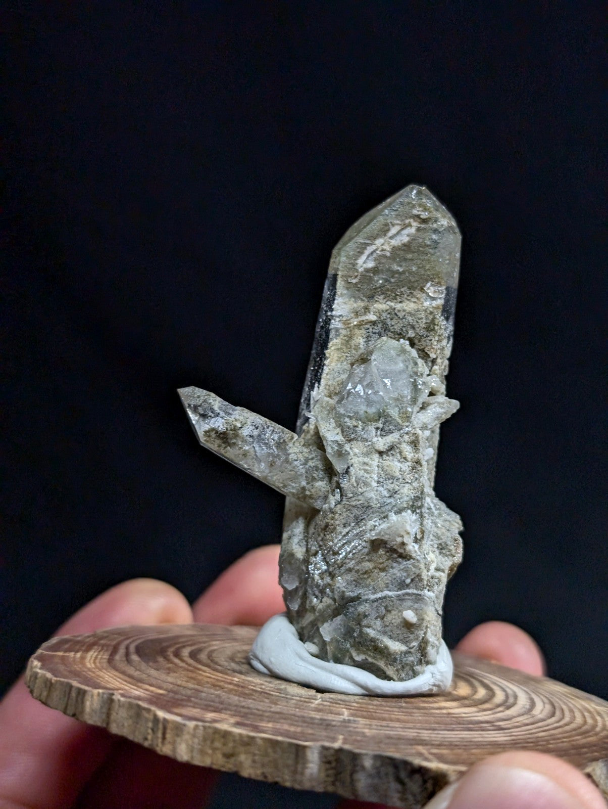 A translucent, grayish quartz crystal cluster with a prominent central point and smaller side crystals, mounted on a circular wooden base.