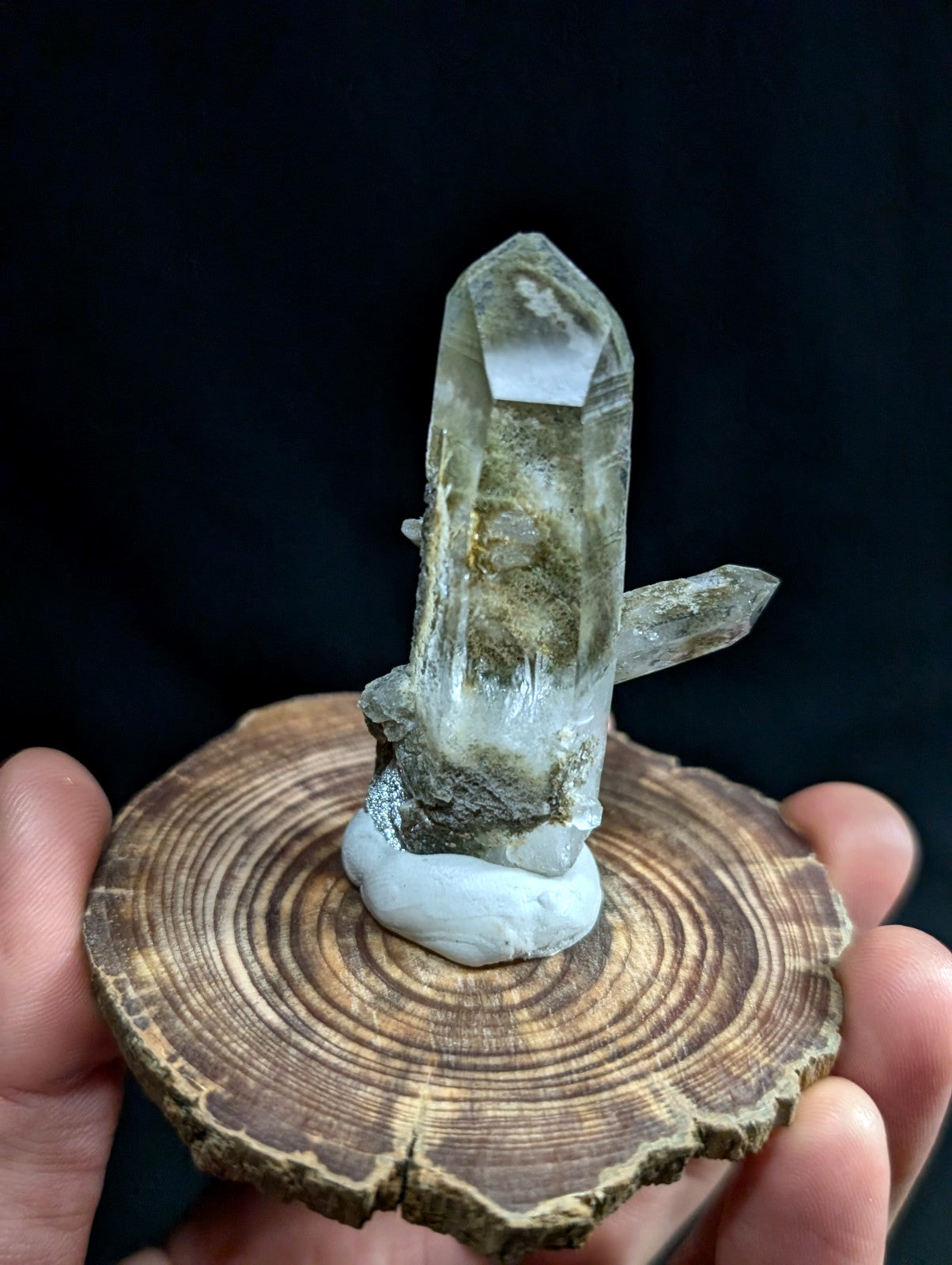 A translucent, greenish-gray quartz crystal cluster with a prominent central point and smaller side crystals, mounted on a circular wooden base.