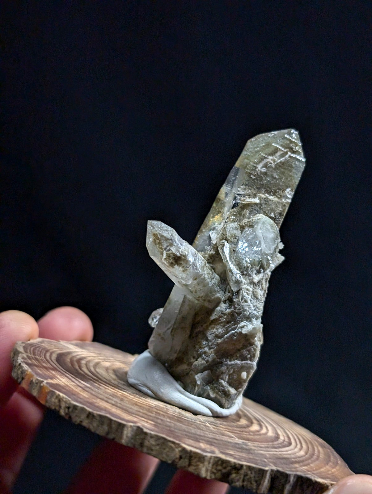 A translucent greenish-gray quartz crystal cluster with a rough, earthy base and sharp, faceted points.