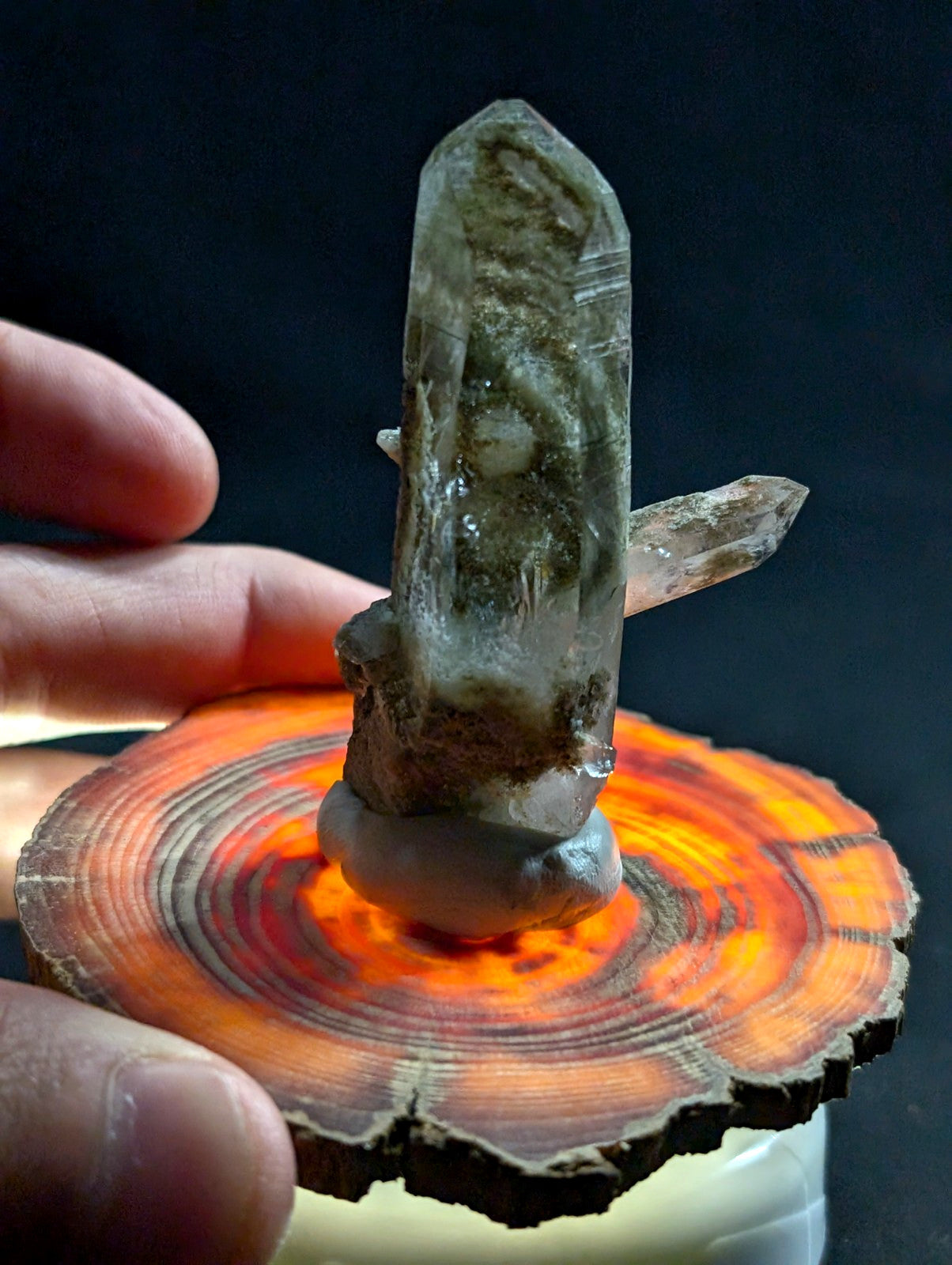 A translucent smoky quartz crystal cluster with a tall, pointed main spike and smaller side crystals, mounted on a circular wooden slice base.