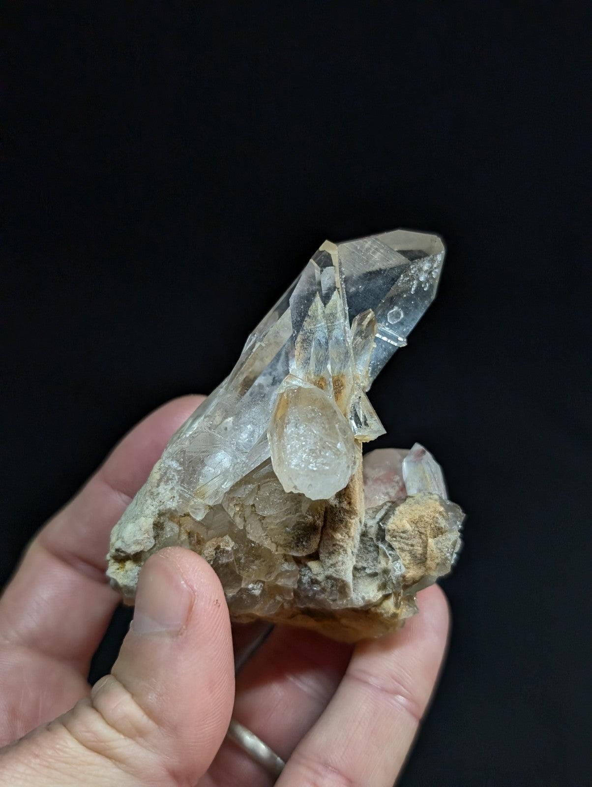 A translucent quartz crystal cluster with clear, pointed facets and a base of earthy brown matrix material.