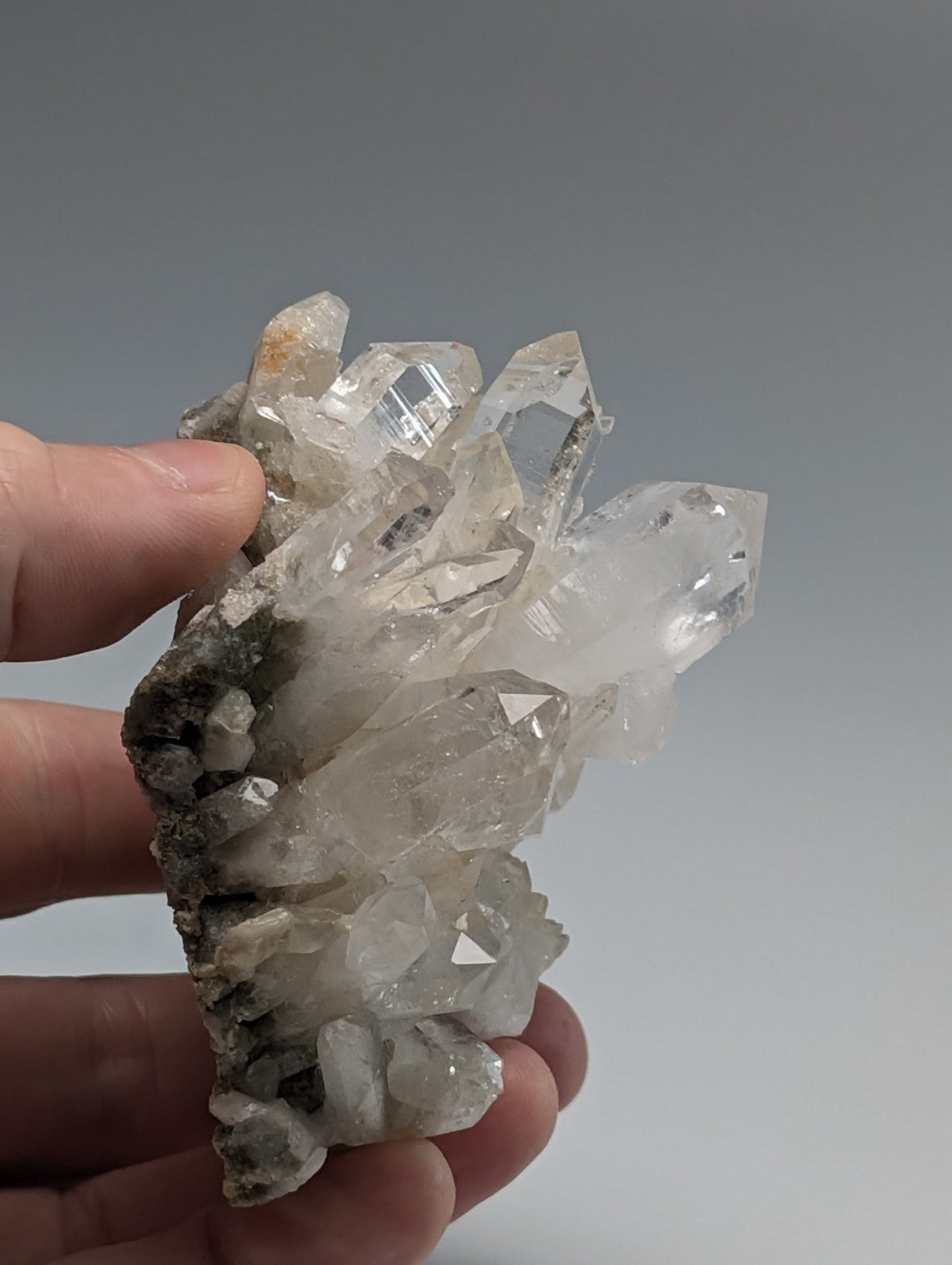 A hand holds a cluster of clear, faceted quartz crystals with some exhibiting subtle golden inclusions and others displaying faint gray veining.