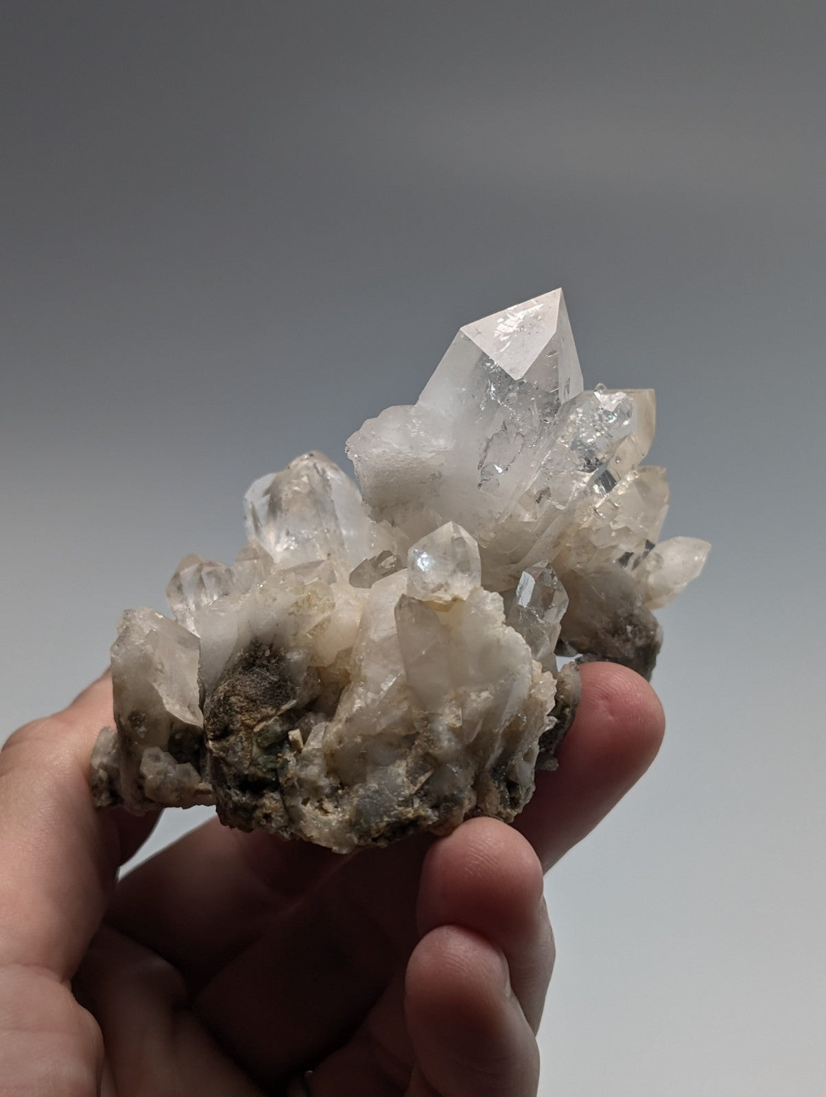 A cluster of clear, faceted quartz crystals growing from a dark, rocky base.
