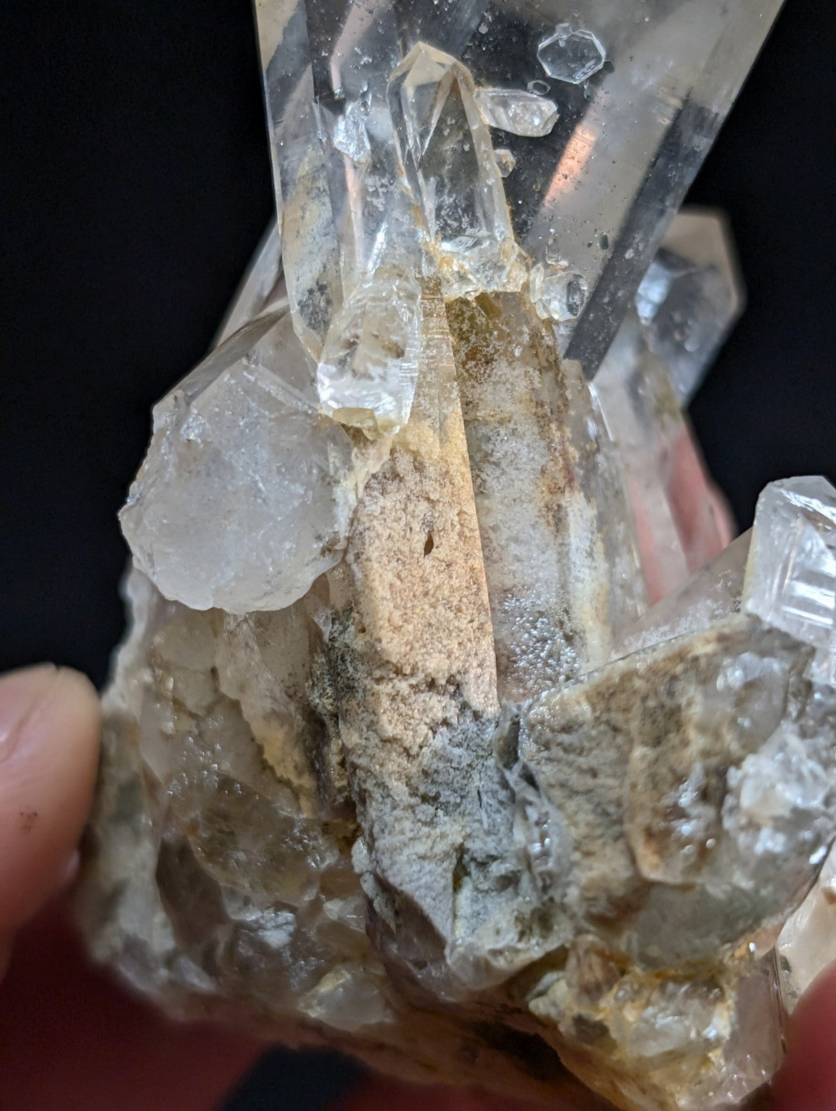 A clear quartz crystal cluster with transparent, faceted points and a base of earthy gray and tan matrix rock.