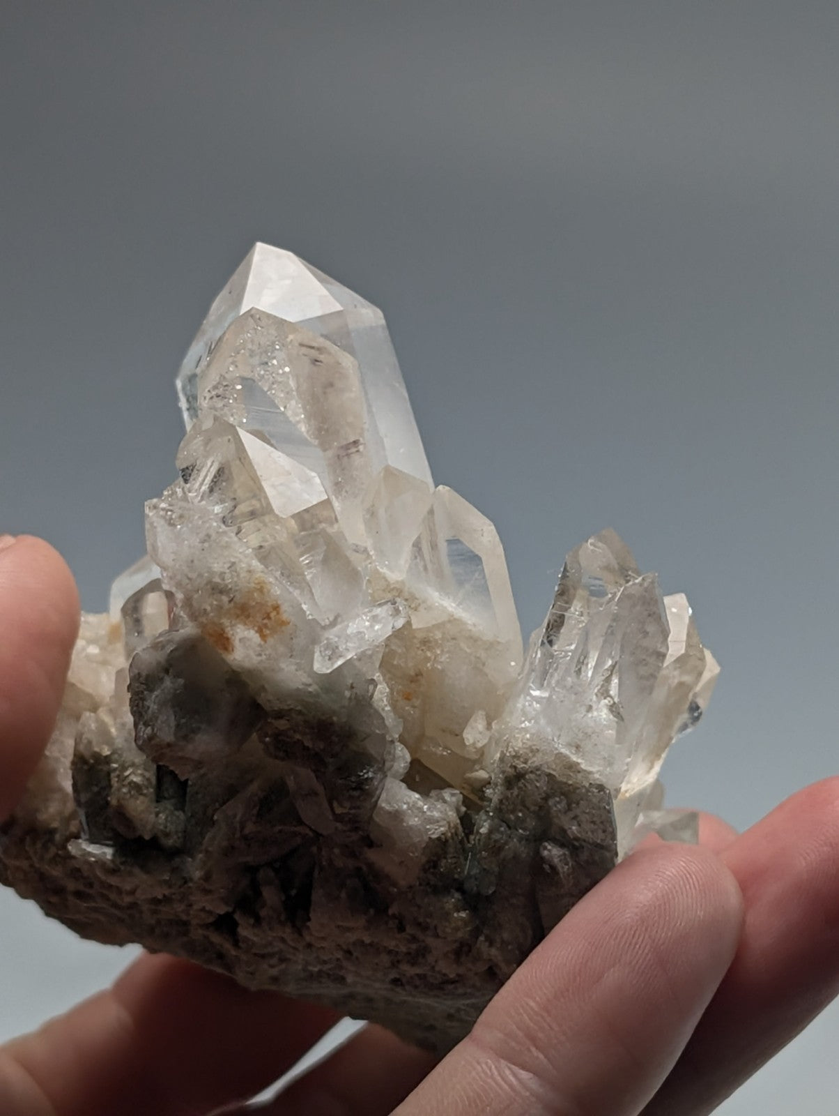 A clear quartz crystal cluster with sharp, faceted points emerging from a rough, earthy matrix.